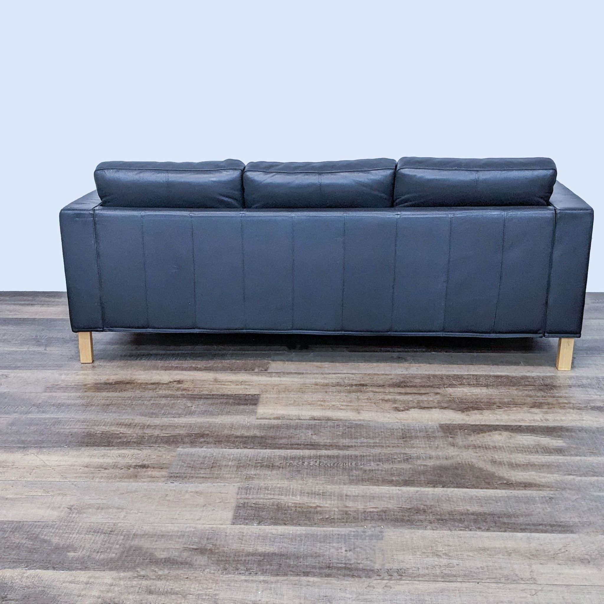 Rear view of a 3-seat black sofa by Reperch with visible seams and wooden legs.