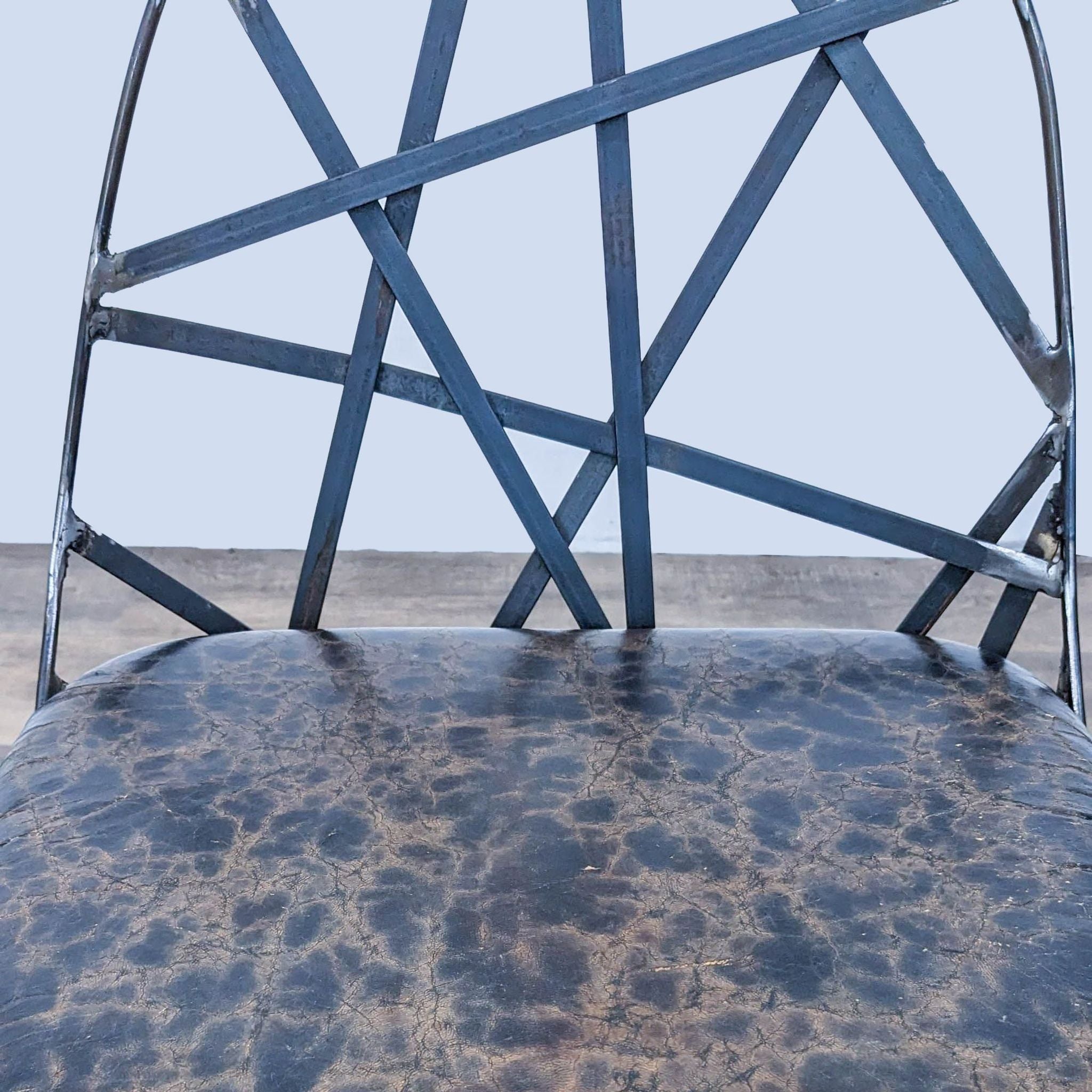 Close-up of Reperch stool's abstract metal frame and textured leather seat, against a neutral background.