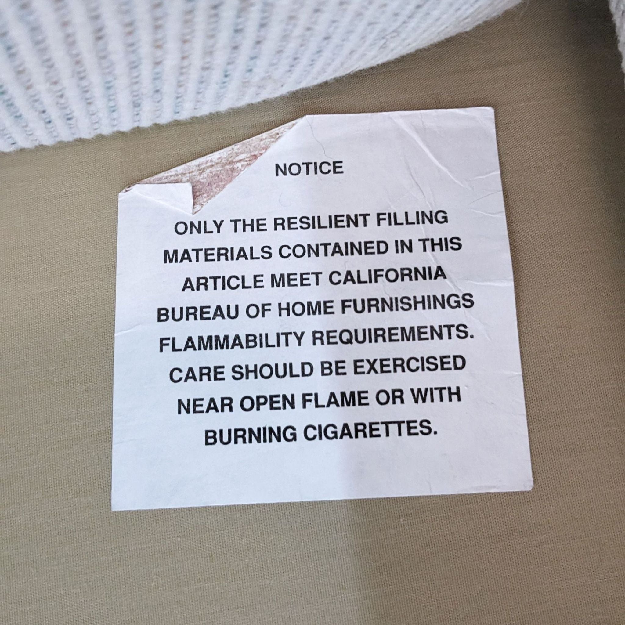 3. A visible warning label on a sofa cushion detailing flammability guidelines and the use of resilient filling materials.