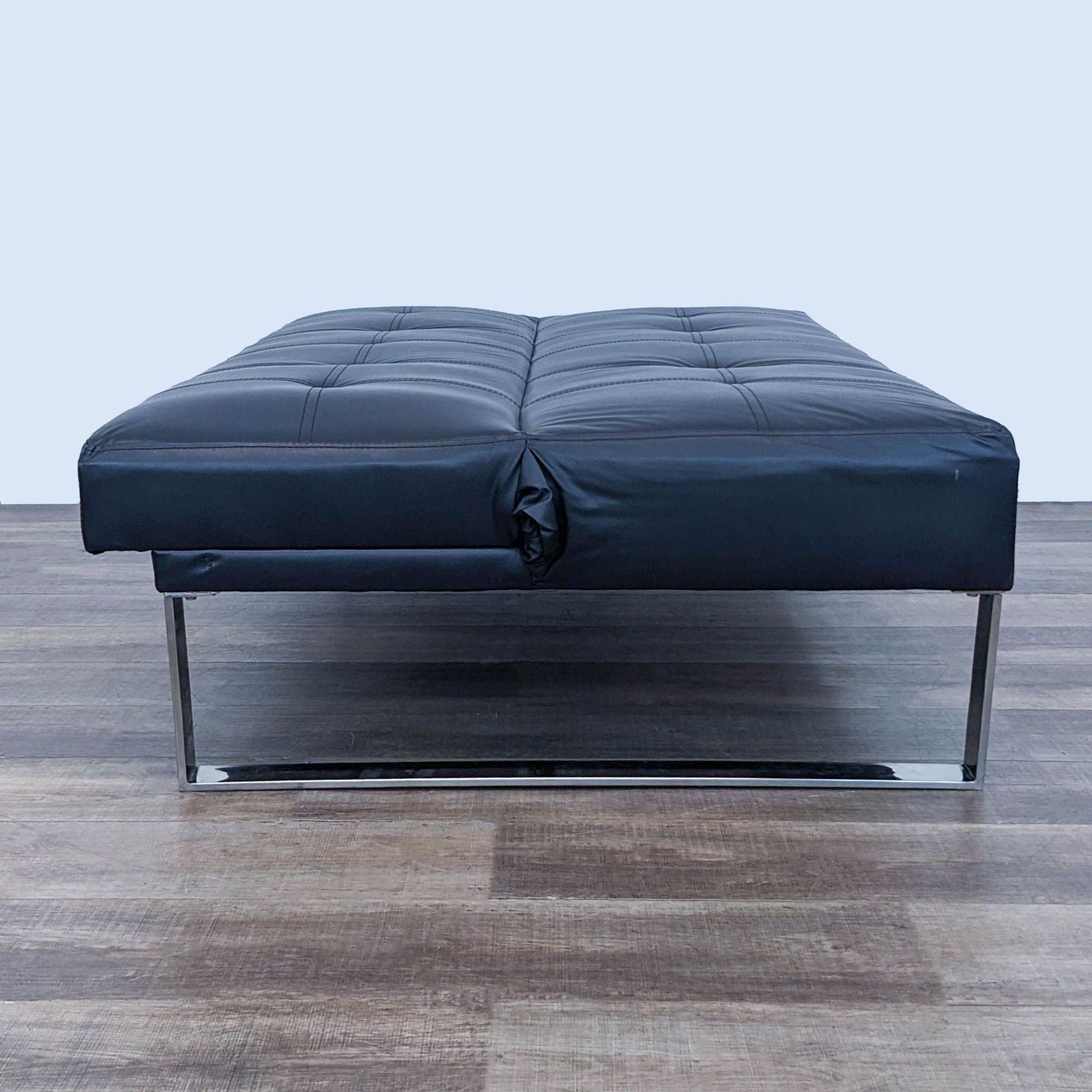 a black leather ottoman with chrome legs and a chrome frame.