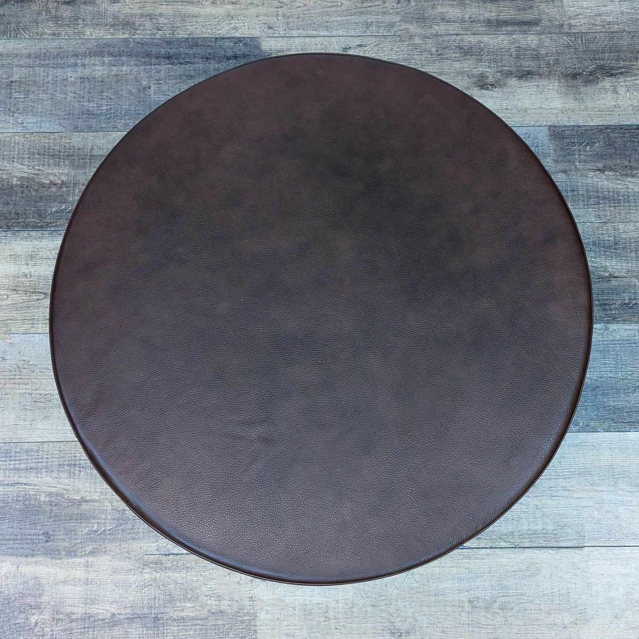 Side view of Room & Board brown round coffee table on wood floor.  