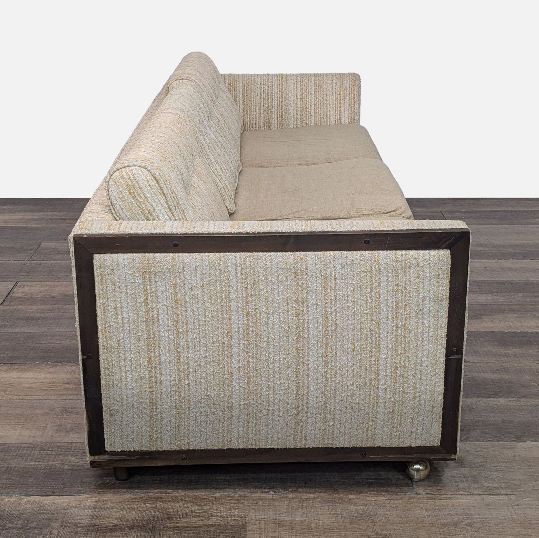 Side view of vintage cream fabric sofa with wood frame and caster wheels, 3-seat, by Connolly's.
