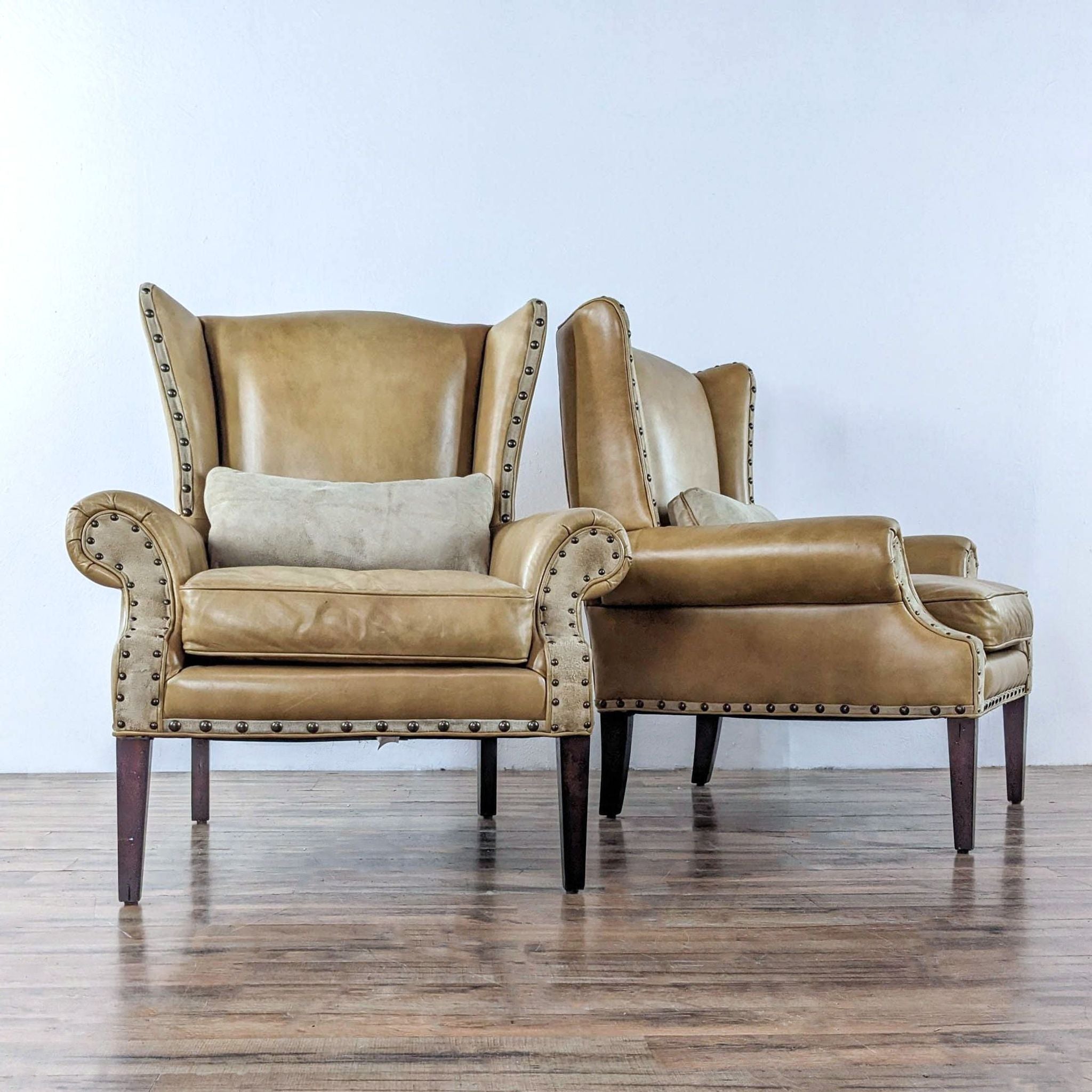 Two Barclay Butera Lifestyle wingback chairs in profile, tan leather with large nailhead accents on arms and base.
