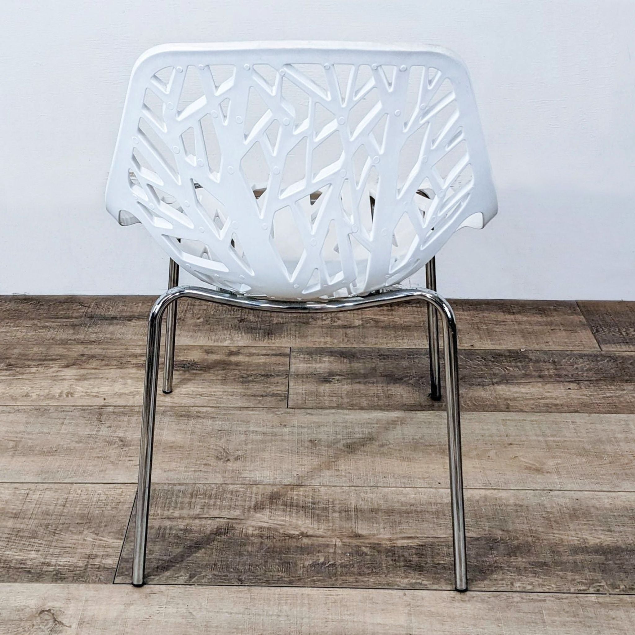 Front view of a modern Reperch white dining chair with a unique cut-out pattern and metallic legs, positioned on a wood-finish floor.