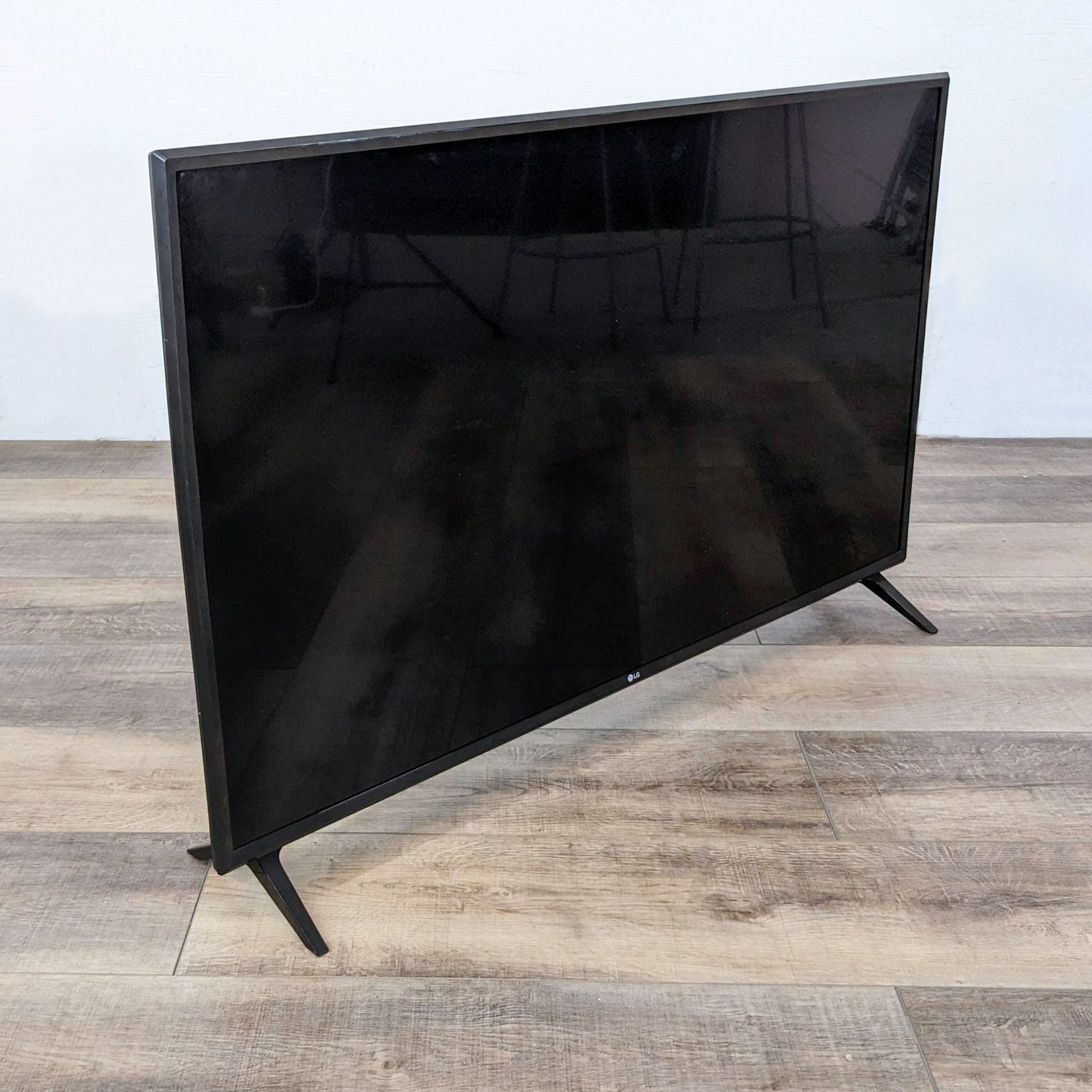 LG brand TV shown from a side angle highlighting its thin profile, on a wooden floor against a white wall.