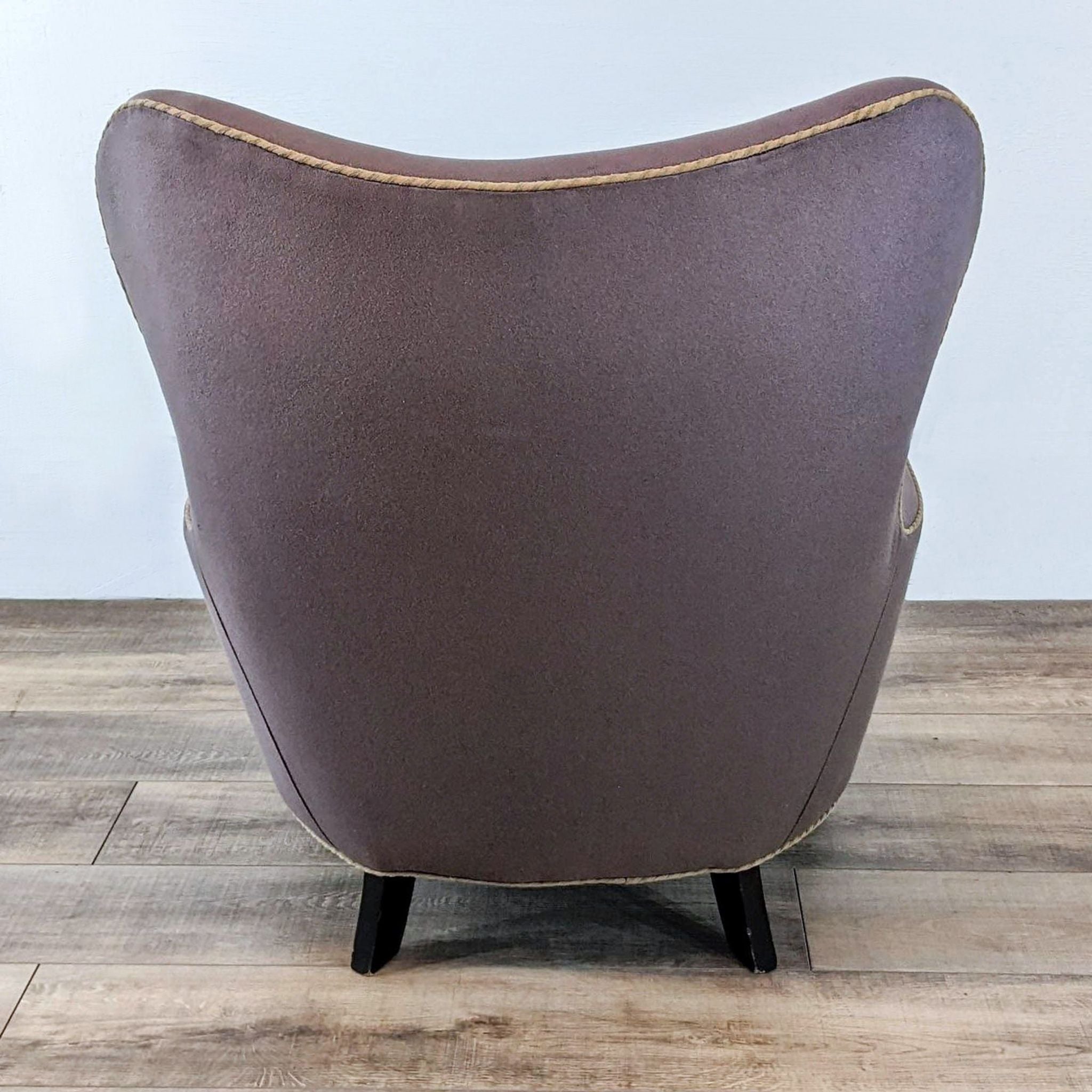 Rear view of a RomI mini chair by Cisco Brothers, showing curved lines with contrasting piping and boot casters.