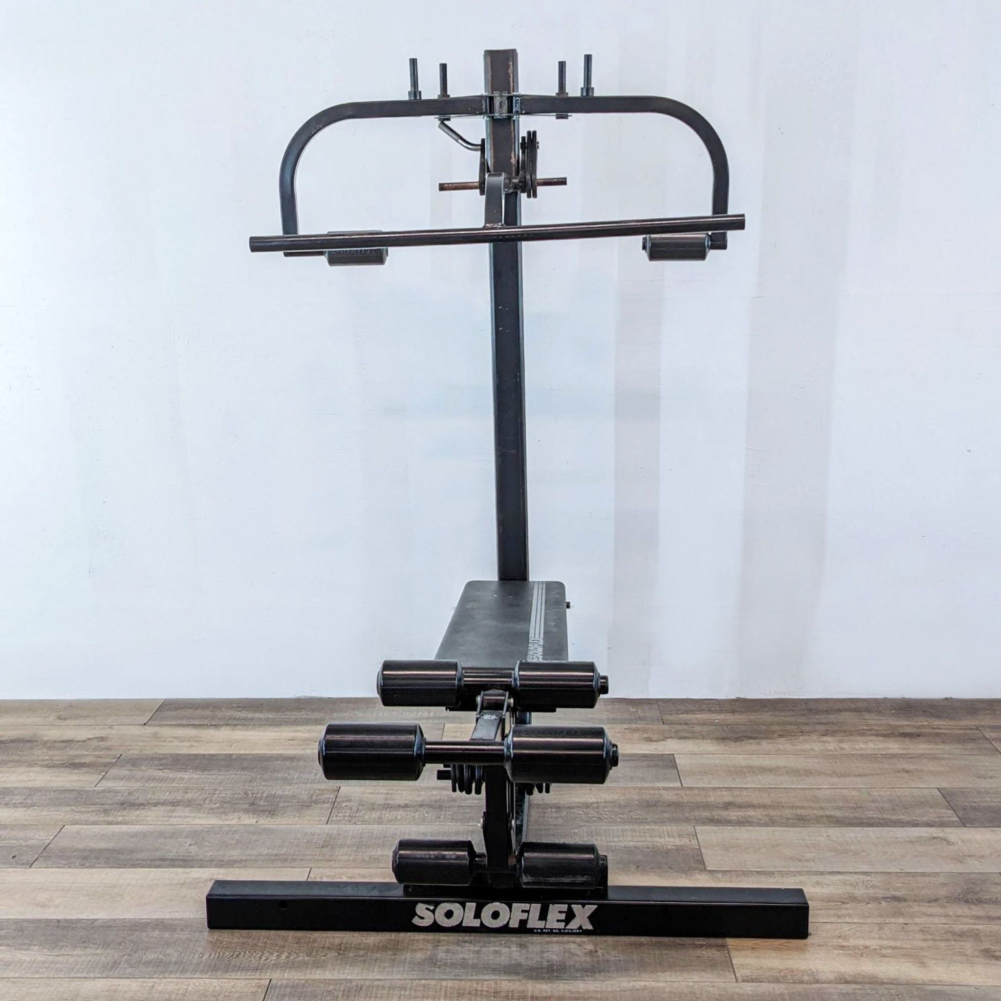 Alt text 1: A Soloflex weightlifting machine with a black bench and resistance bar arms against a white wall.