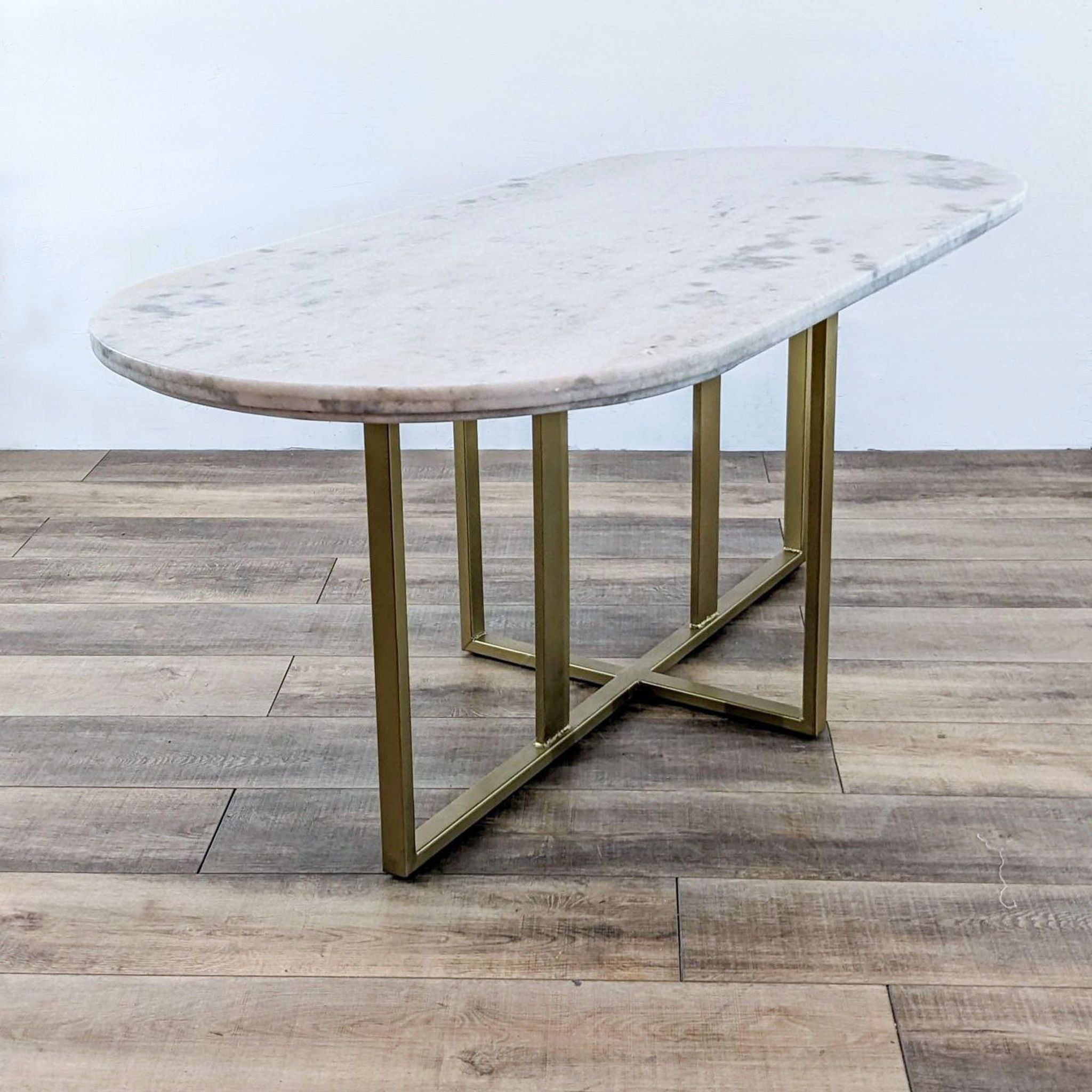 Alt text 2: Frontal angle of a Four Hands Dylia table, displaying its white marble surface and clean-lined brass base on a wood-patterned floor.