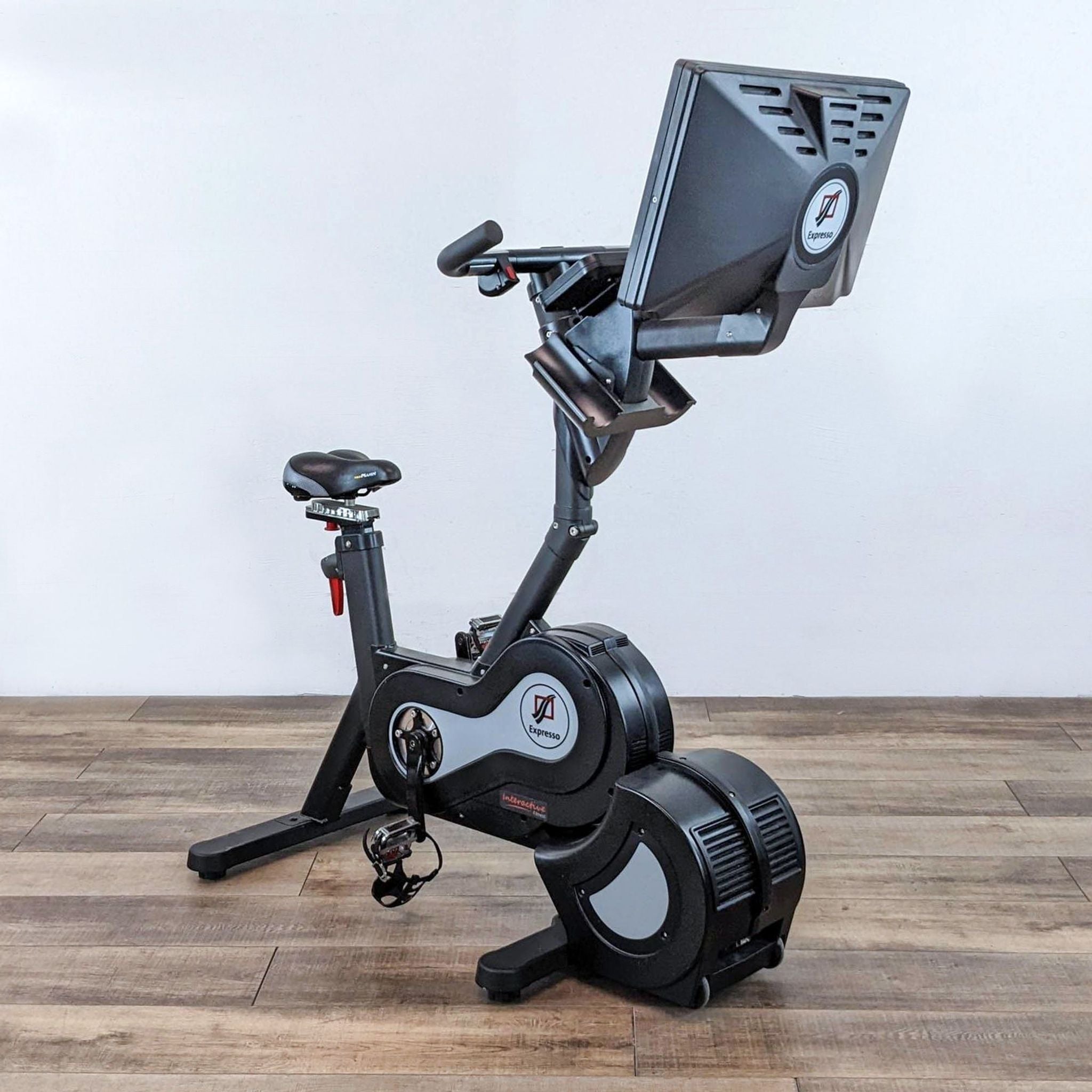 Expresso brand stationary bike with a large screen and black frame on a wooden floor.