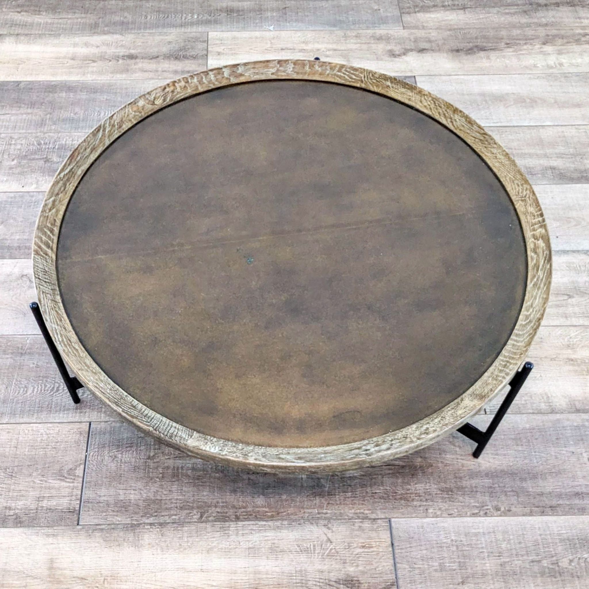 Top-down view of a round wooden Pottery Barn coffee table with a rustic finish, contrasting with the wooden floor beneath.
