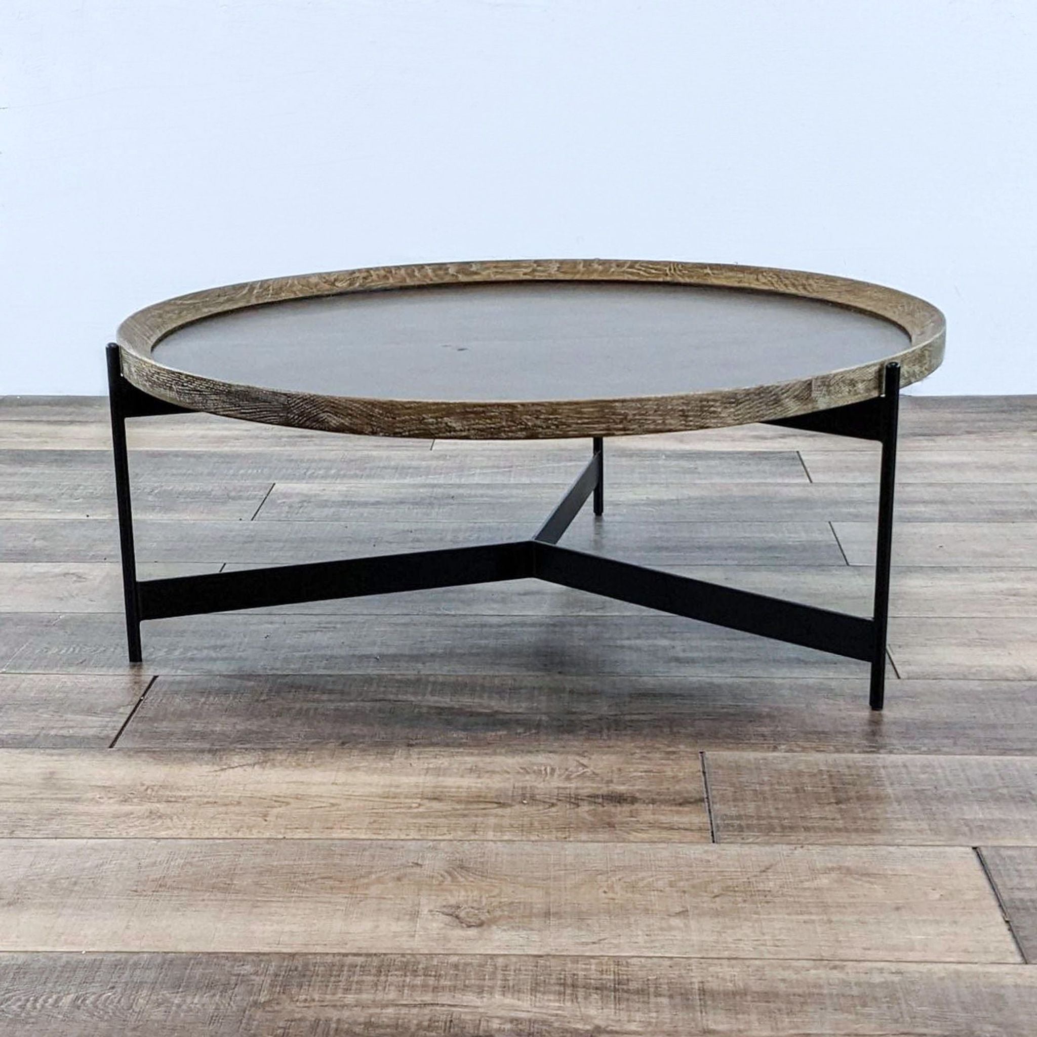 Round Pottery Barn coffee table with textured wooden top and angled black metal legs on a wooden floor.