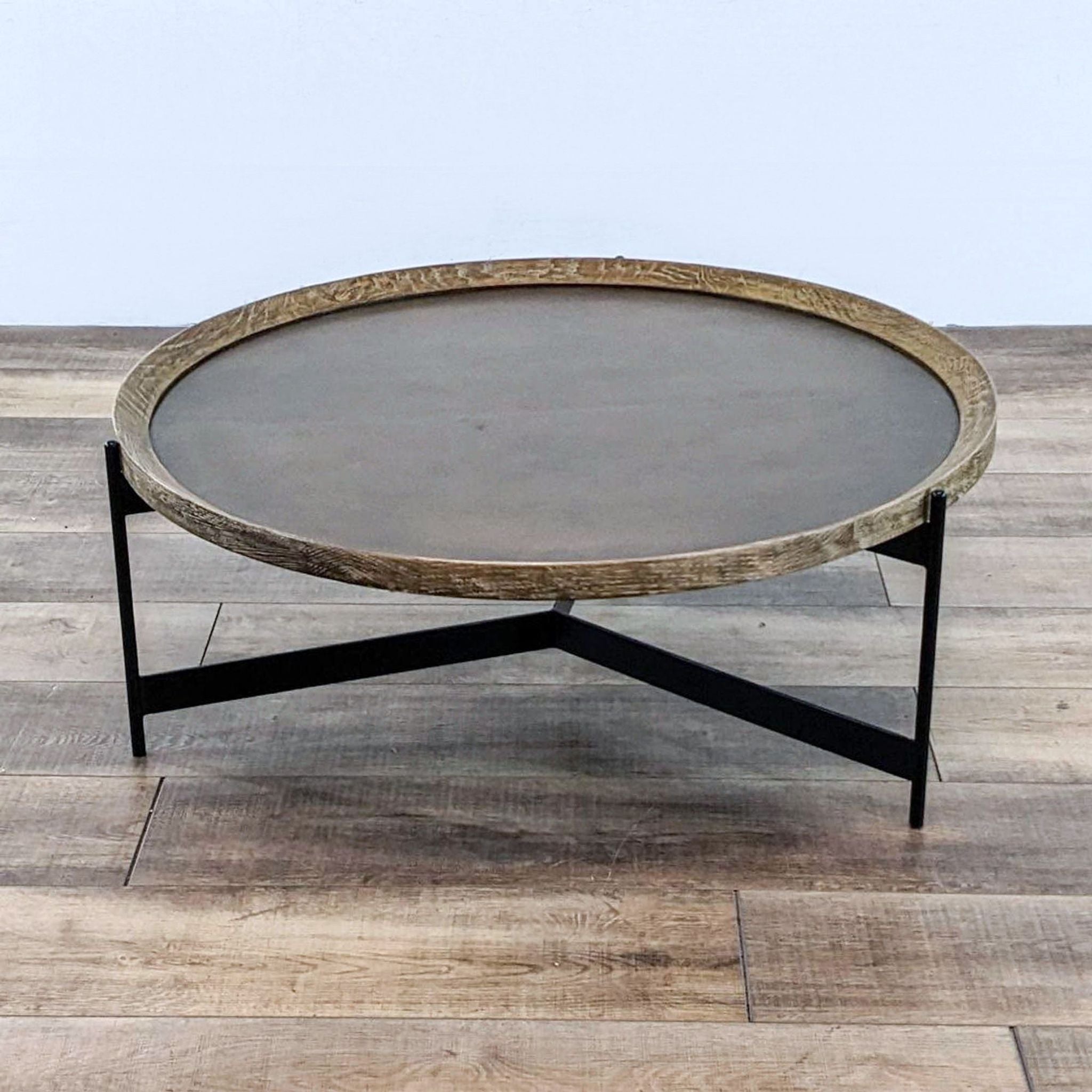 Round Pottery Barn coffee table with textured edge and black angular legs on a wood floor.