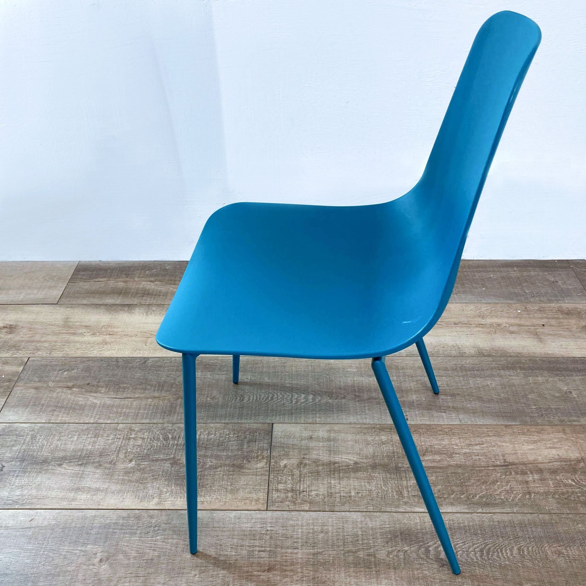 Side view of a Reperch modern teal plastic molded chair with durable metal legs on wooden flooring.