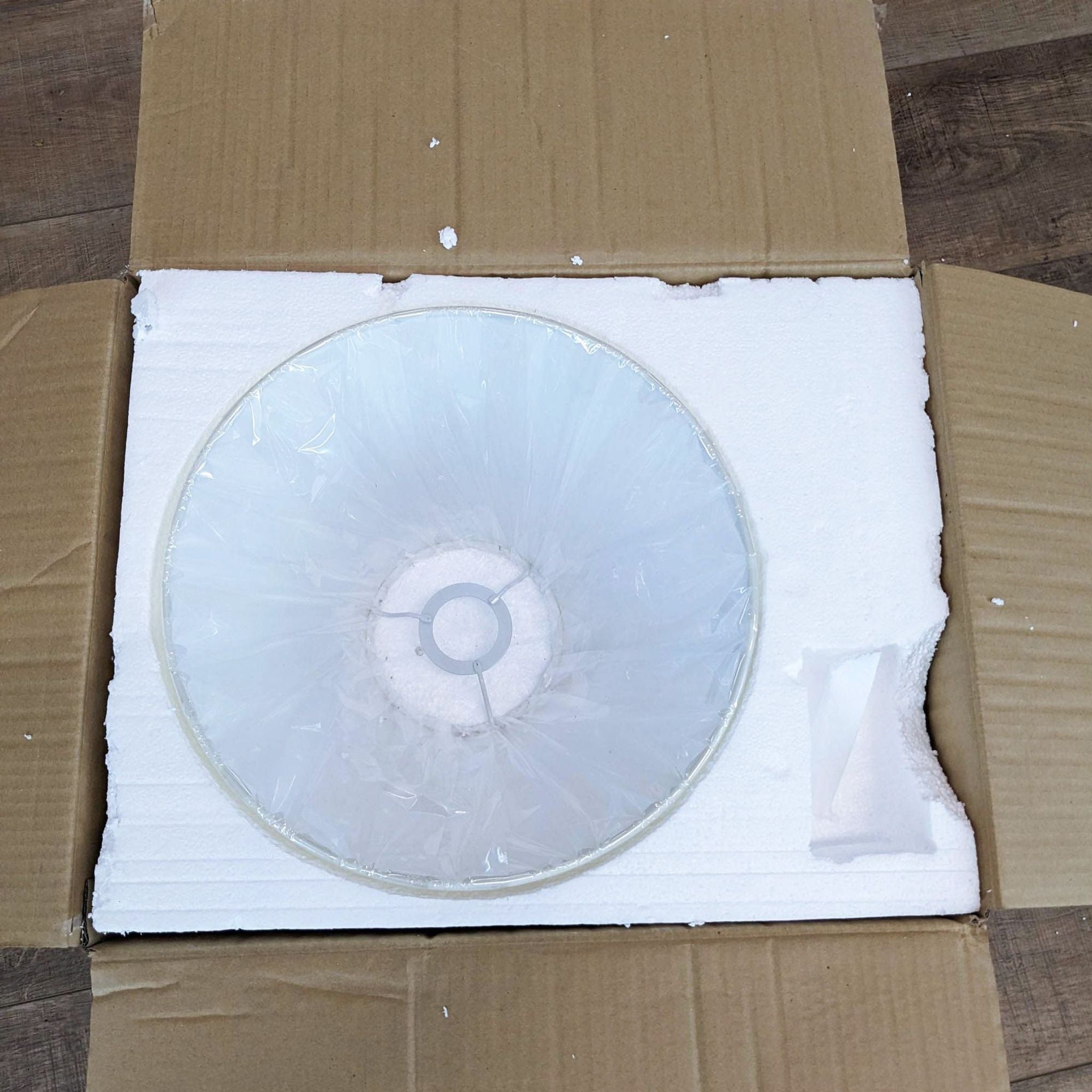Round lampshade wrapped in plastic, part of a Ralph Lauren light by Visual Comfort, unpacked on cardboard.