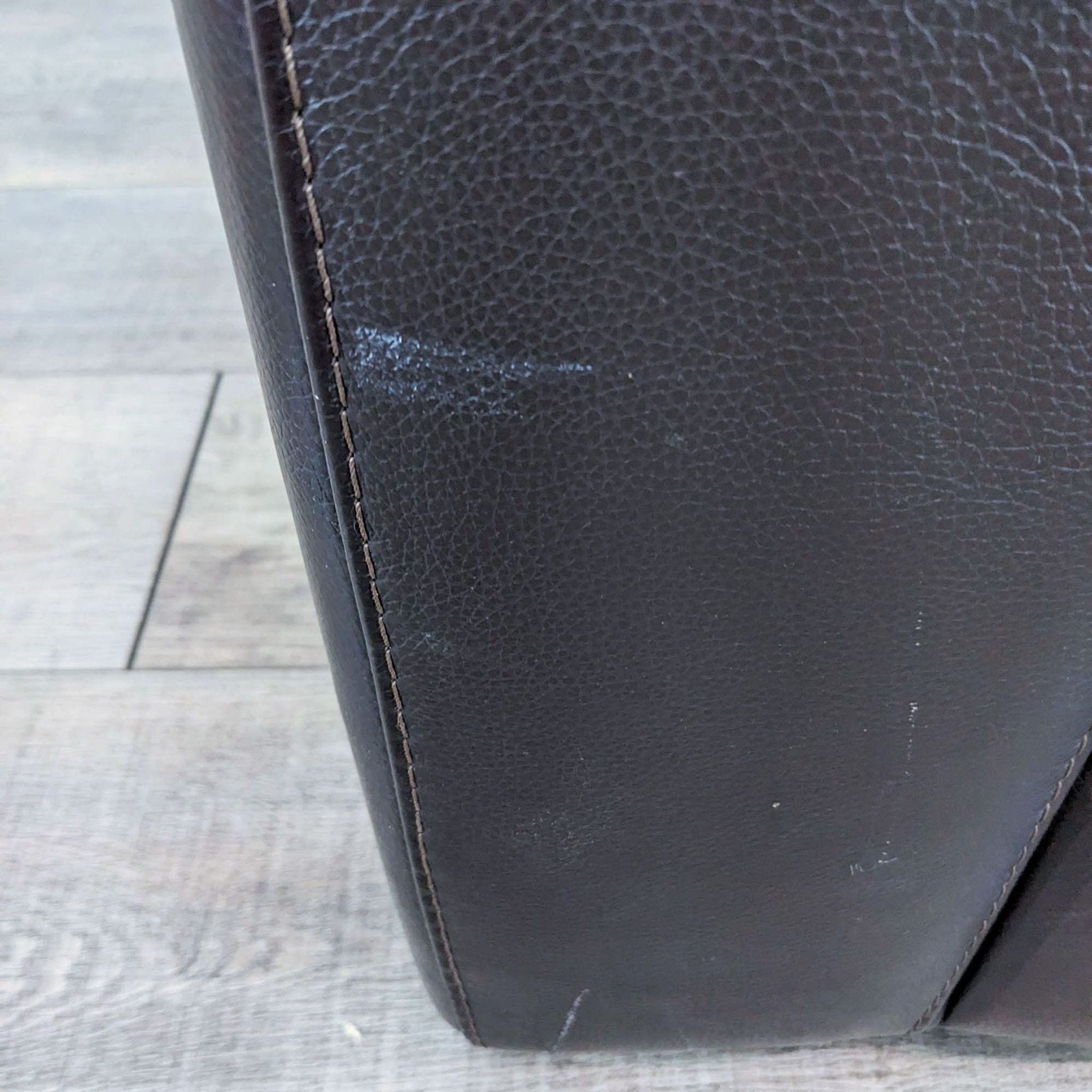 Close-up of the corner of a Domicil leather lounge chair showing wear on the surface.