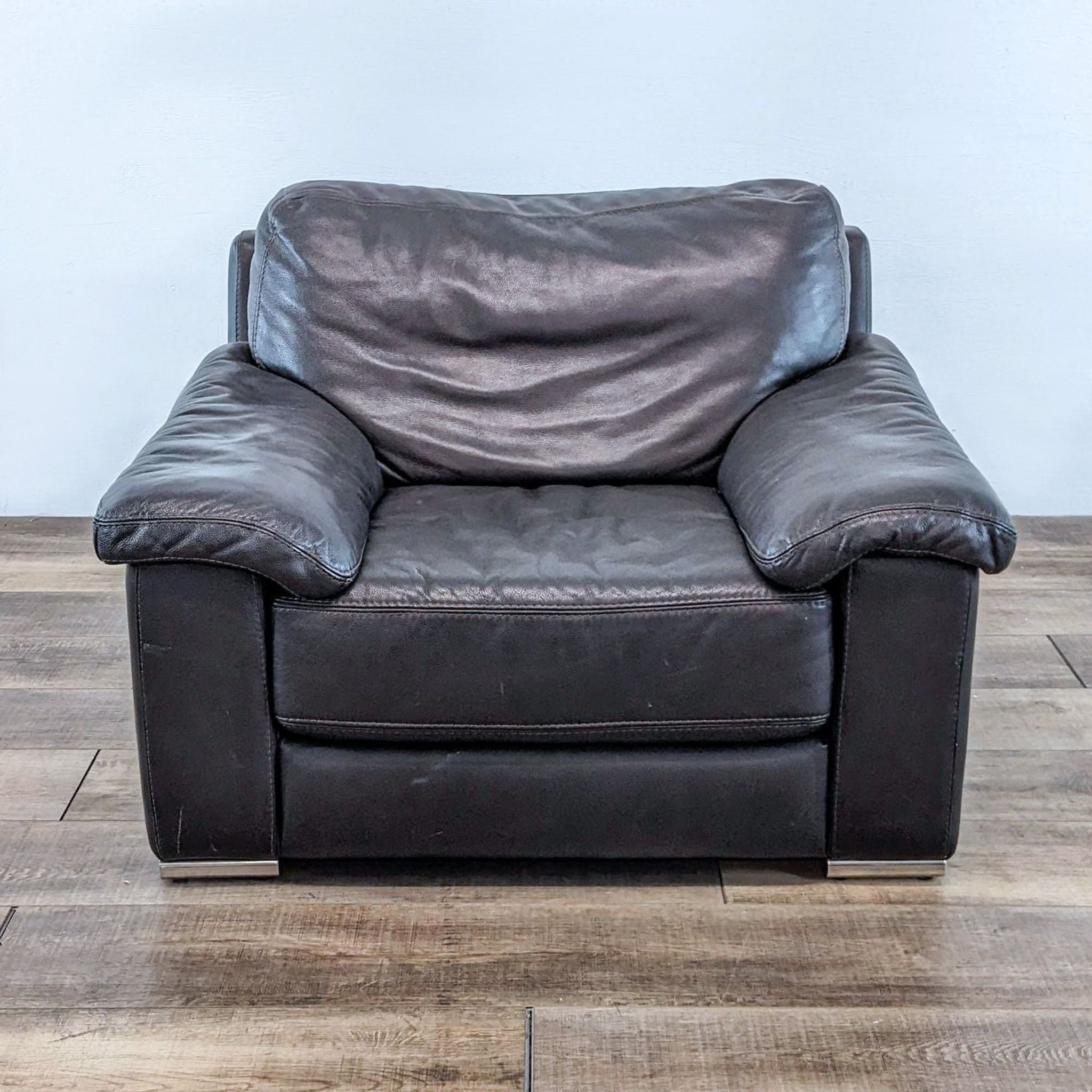 Front view of a Domicil leather lounge chair with a plush design, against a wooden floor and white wall.