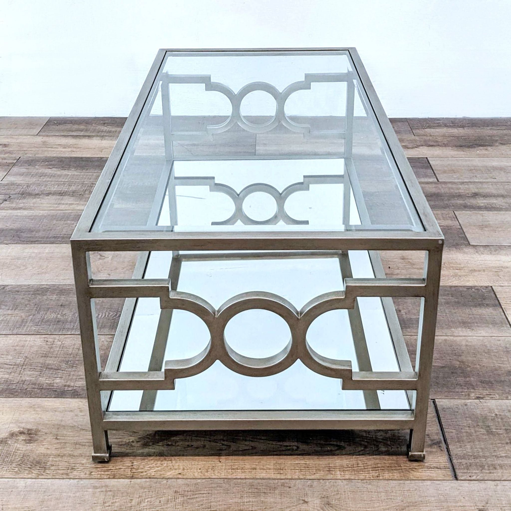 Neiman Marcus coffee table with metal base and mirrored top and shelf, featuring geometric patterns, on a wooden floor.