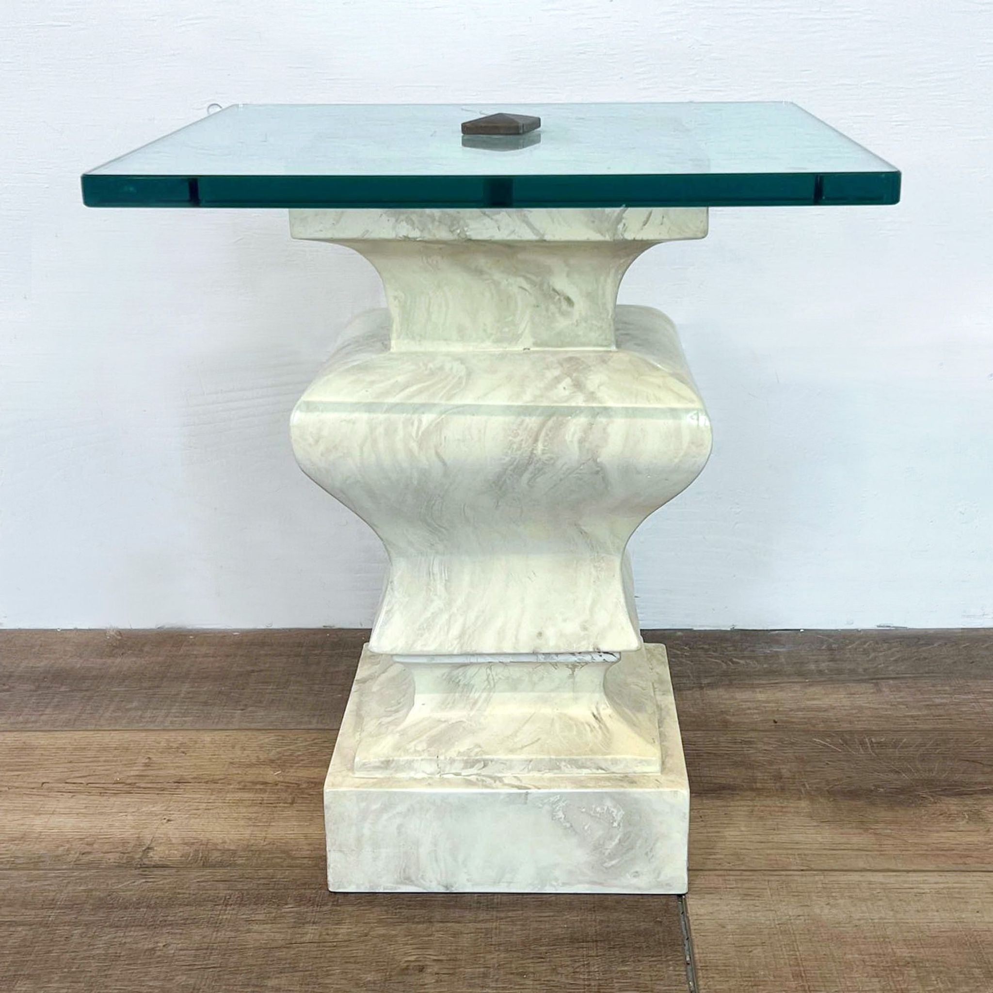 Reperch marble end table with a square, teal tinted glass top and a sculpted base on a wooden floor.