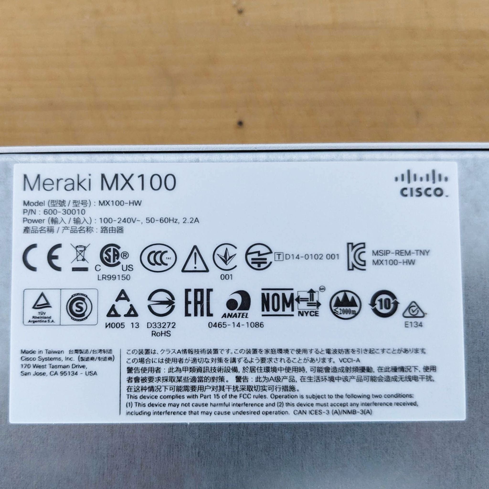 Label sticker of a Cisco Meraki MX100 networking device detailing model information, certifications, and regulatory compliance icons.