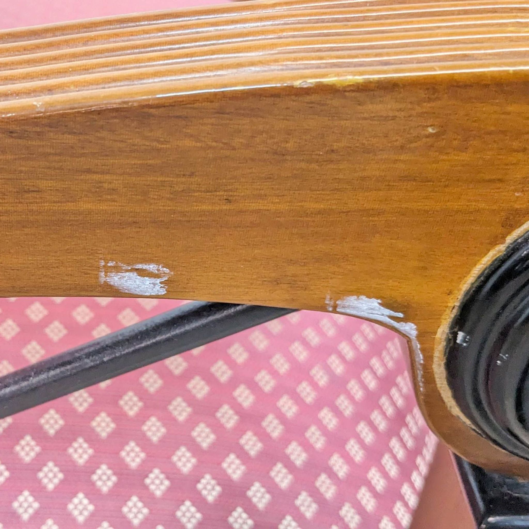 Close-up of Reperch lounge armchair showing wood frame with worn paint and part of the pink upholstered seat with a pattern.