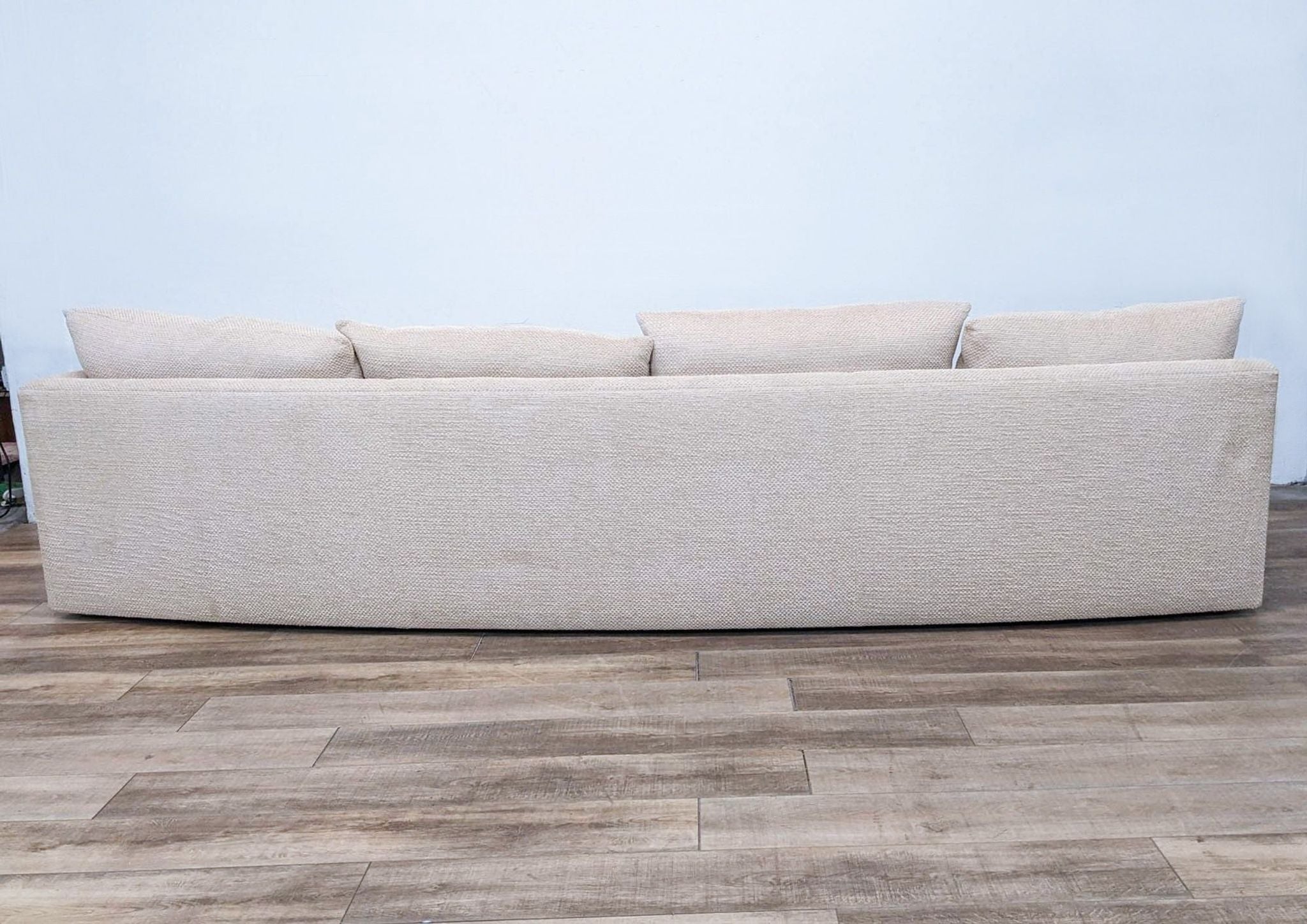 Reperch one-piece curved sectional sofa with one armrest and several cushions, against a plain wall on wooden flooring.