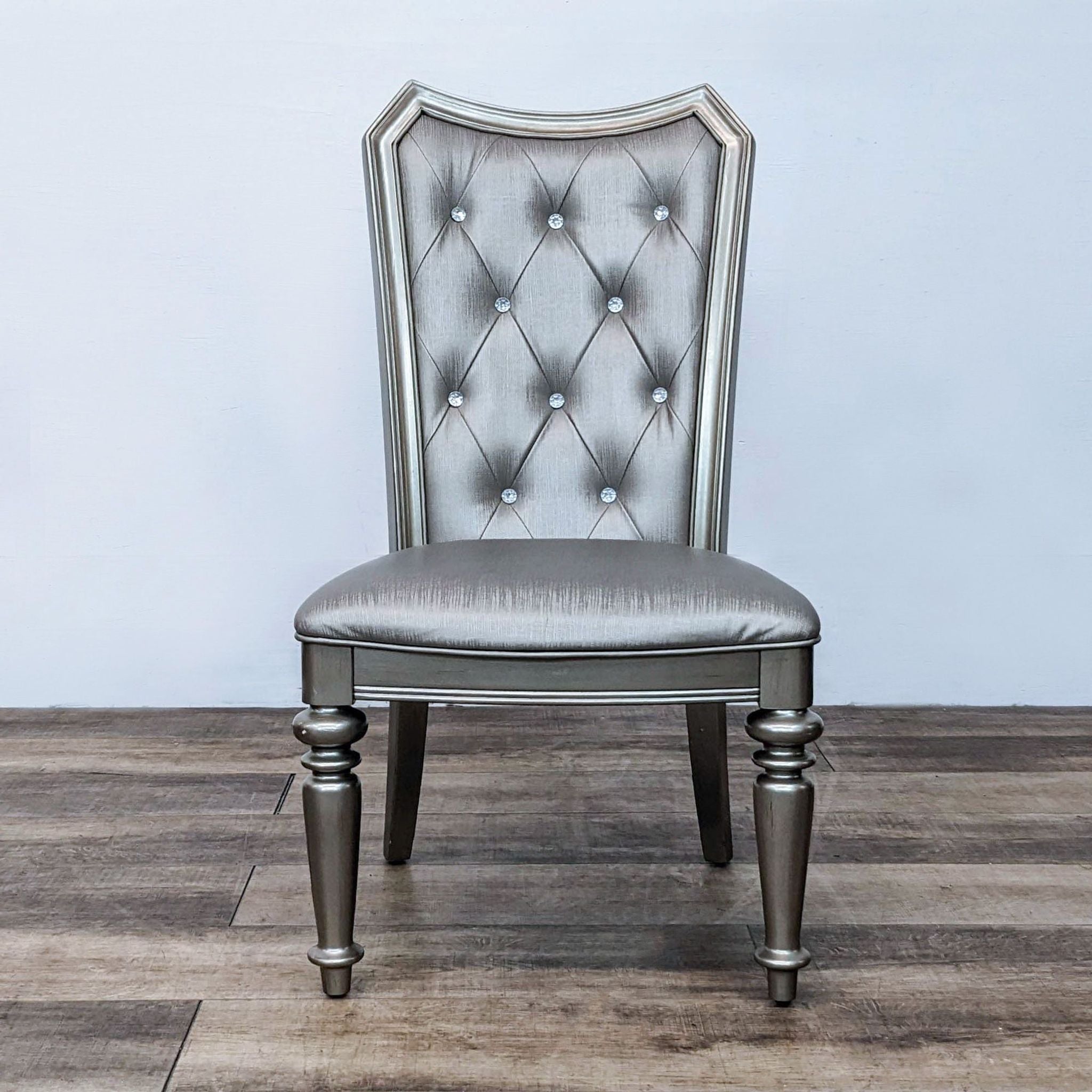 Platinum-finished CoasterEssence dining chair with diamond tufting and crystal buttons on a metallic faux leather upholstery.