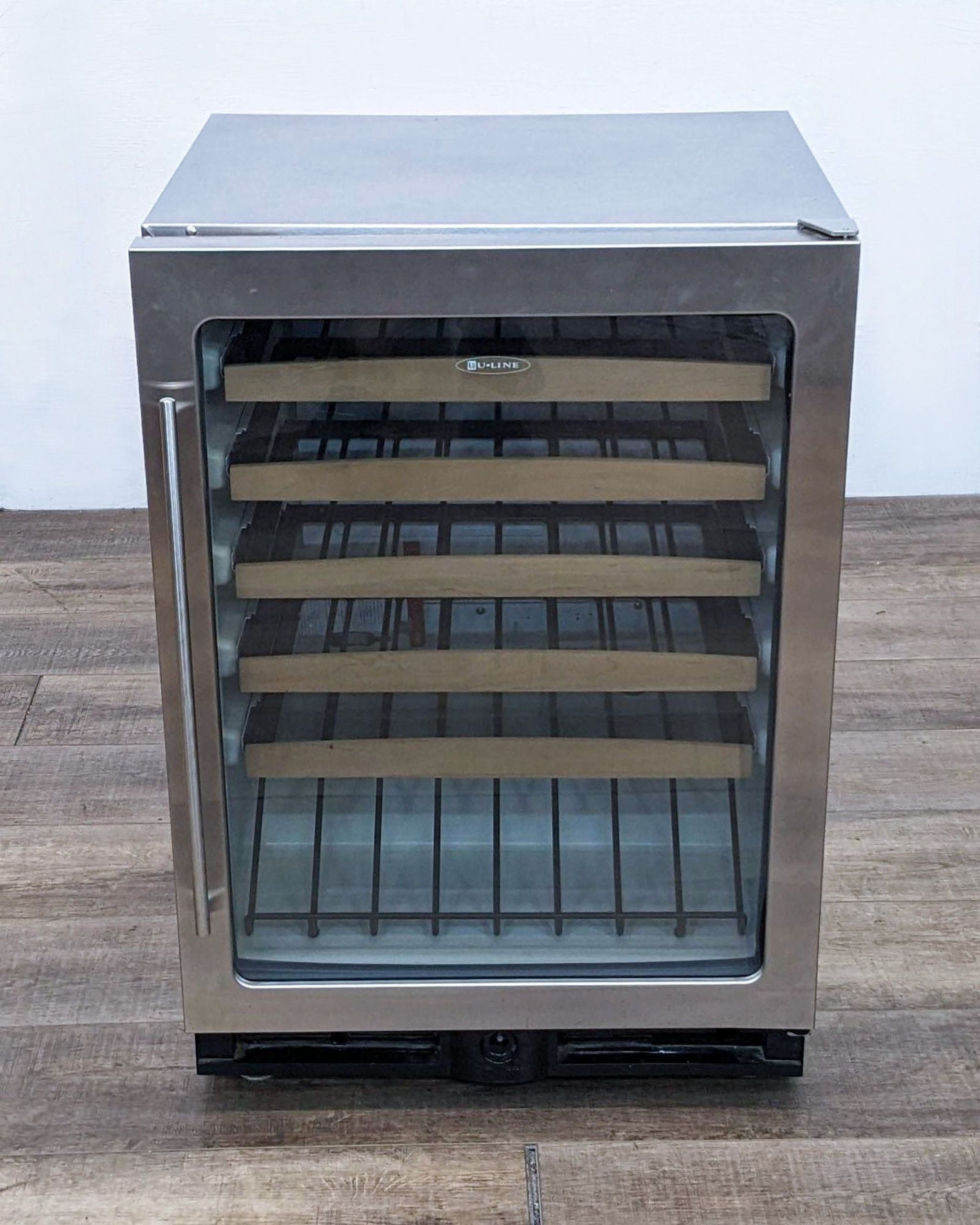 U-Line brand stainless steel refrigerator with glass door and visible shelves, standing on a wooden floor.
