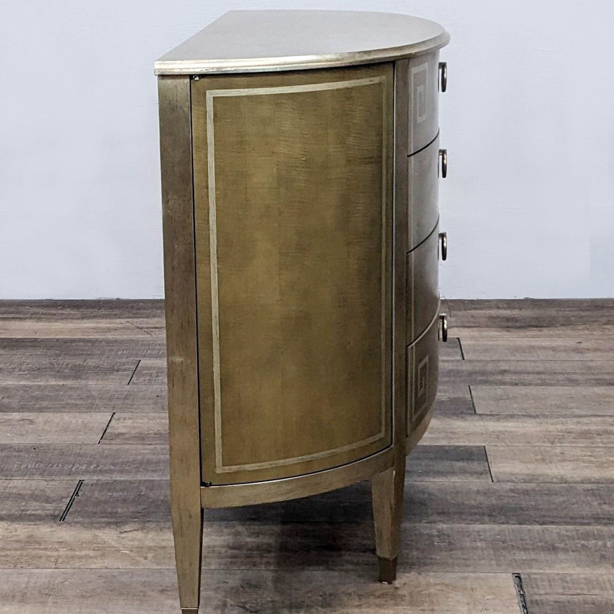 Caracole brand curved cabinet with a gold finish and side drawer detail on wooden flooring.
