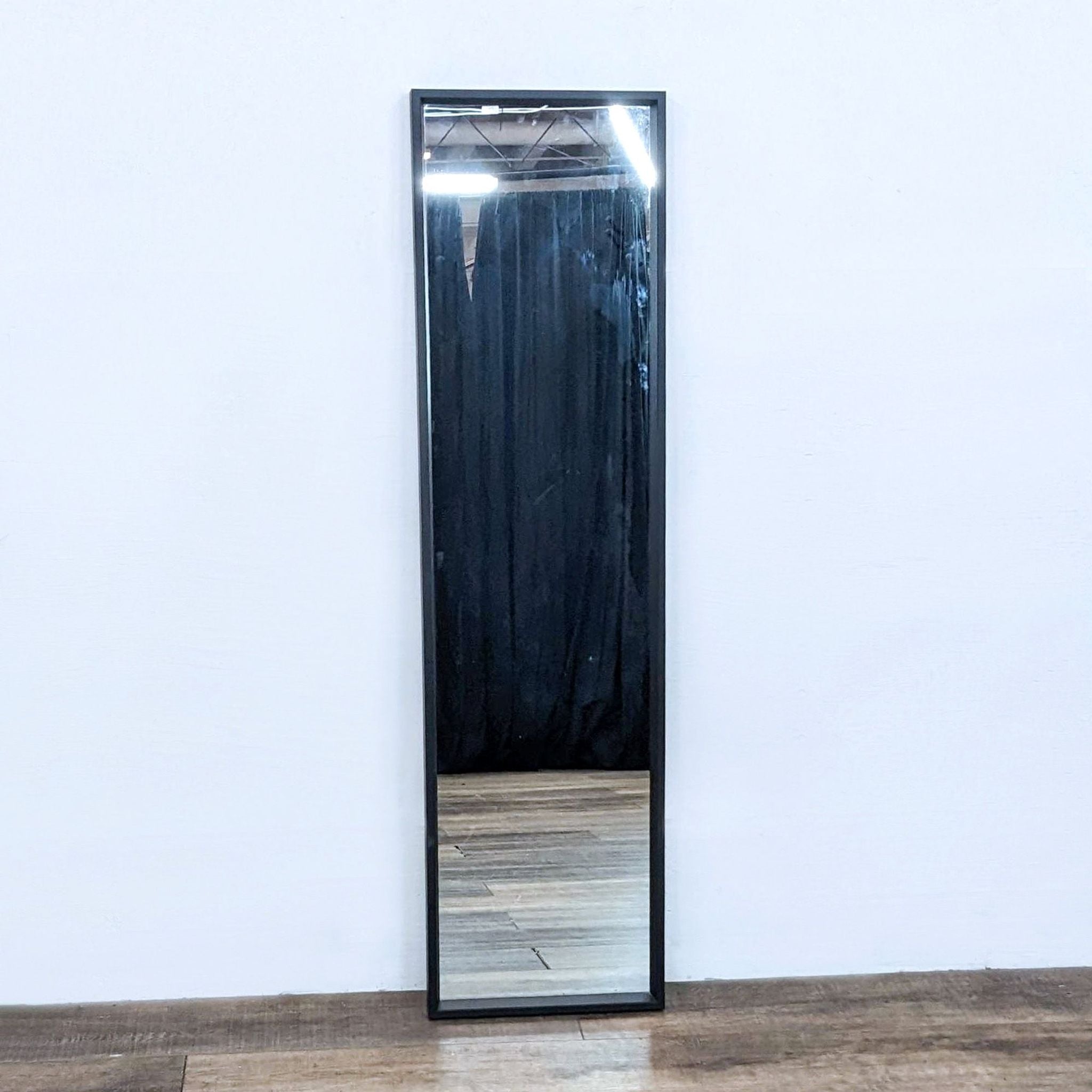 Ikea Nissdal long mirror, vertical position, with black frame against a white wall on wooden flooring.