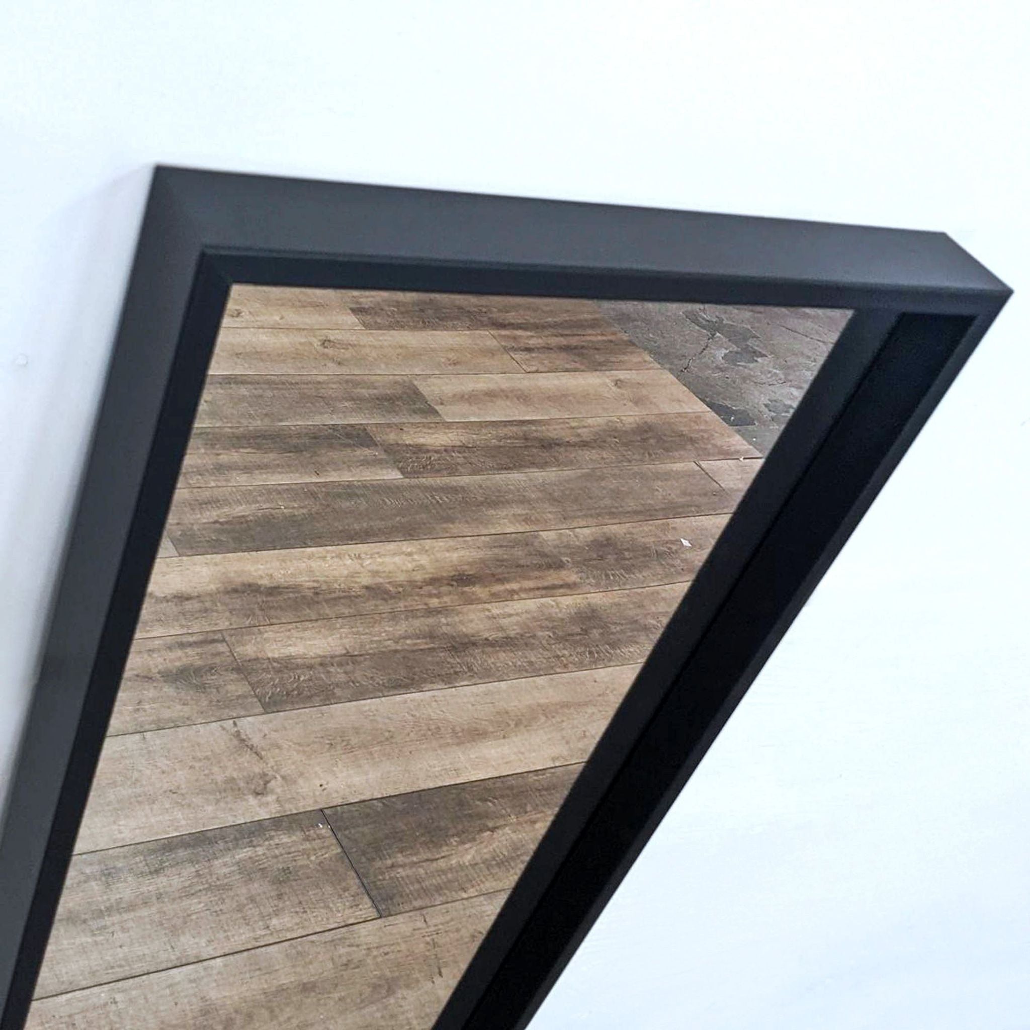 Close-up of Ikea Nissdal mirror's corner showing the black frame's texture and angled view of the wooden floor reflection.