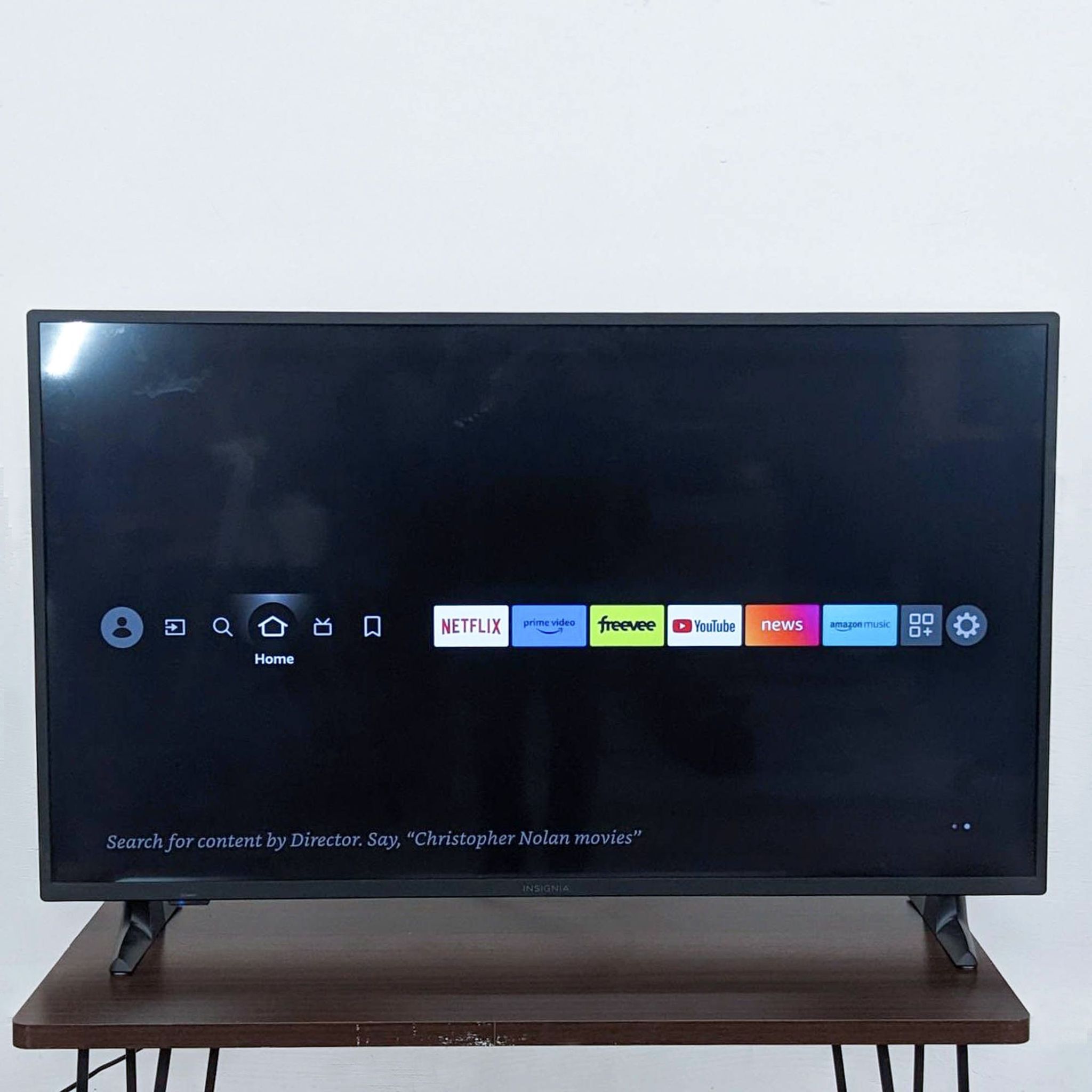 Insignia TV on stand displaying smart interface with streaming apps like Netflix and a search prompt.