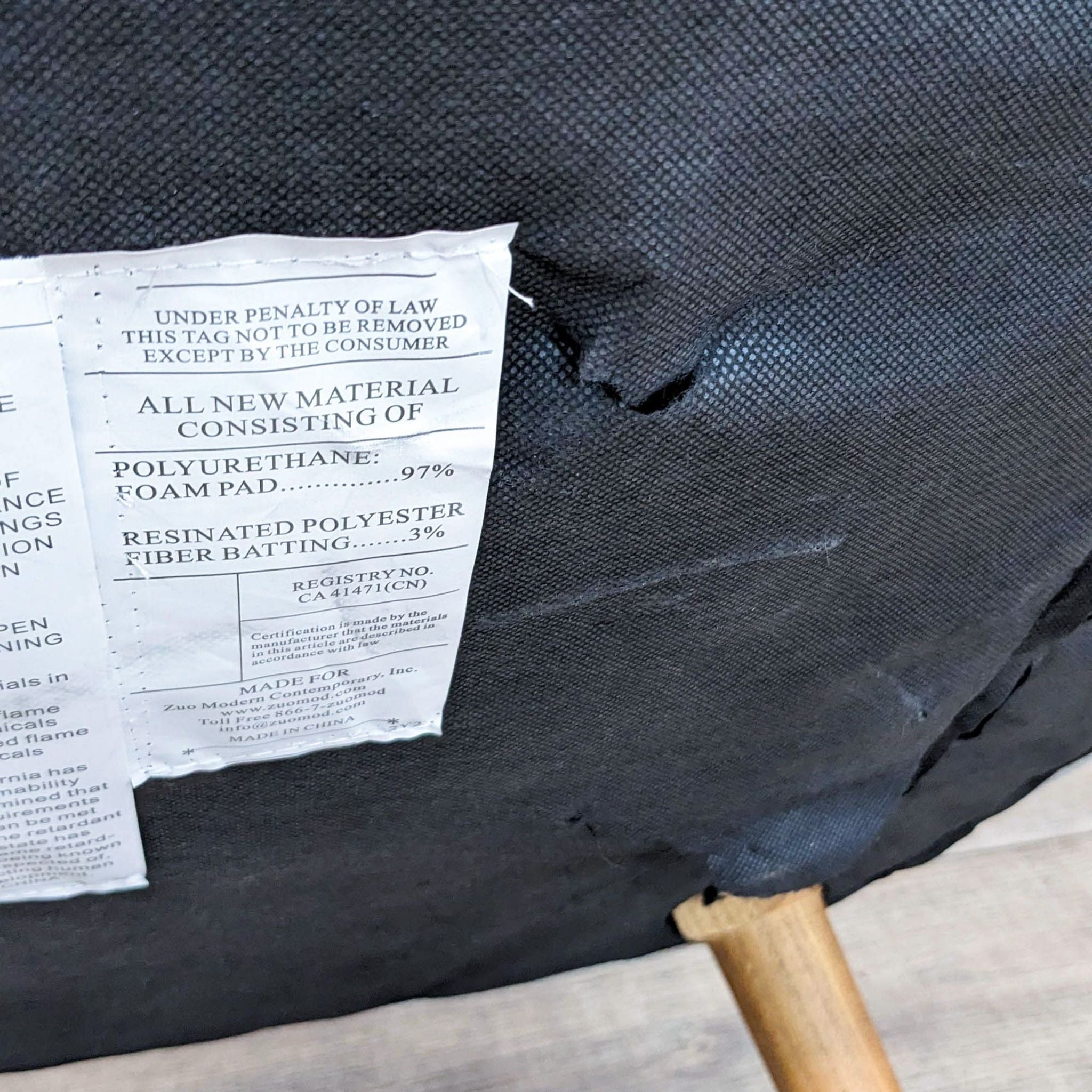 Alt text: Close-up of a Zuo Modern lounge item's law label on black fabric with a visible tear, showing material composition details.