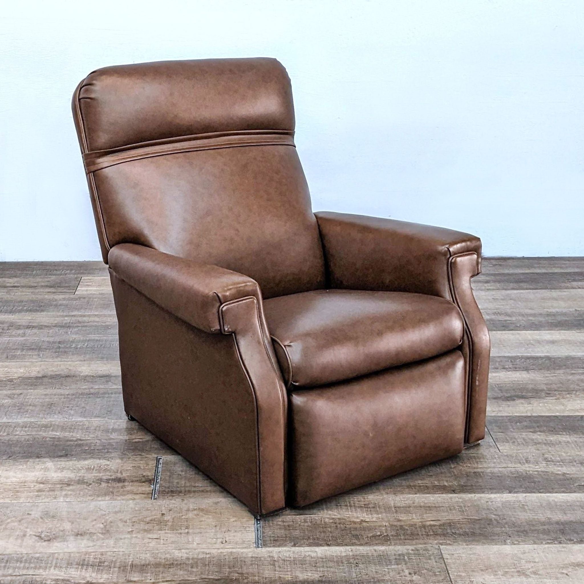 Reperch transitional brown leather recliner with nailhead trim on a wooden floor.