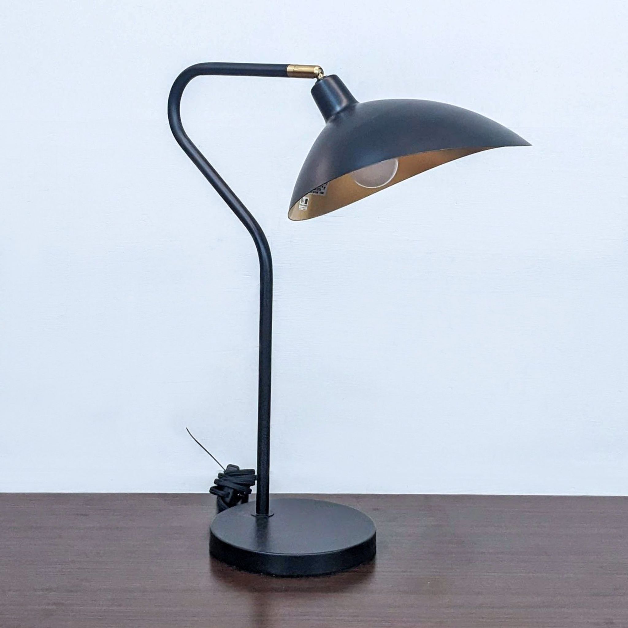 Safavieh mid-century style adjustable table lamp, black with gold accents, off-state on wooden surface.