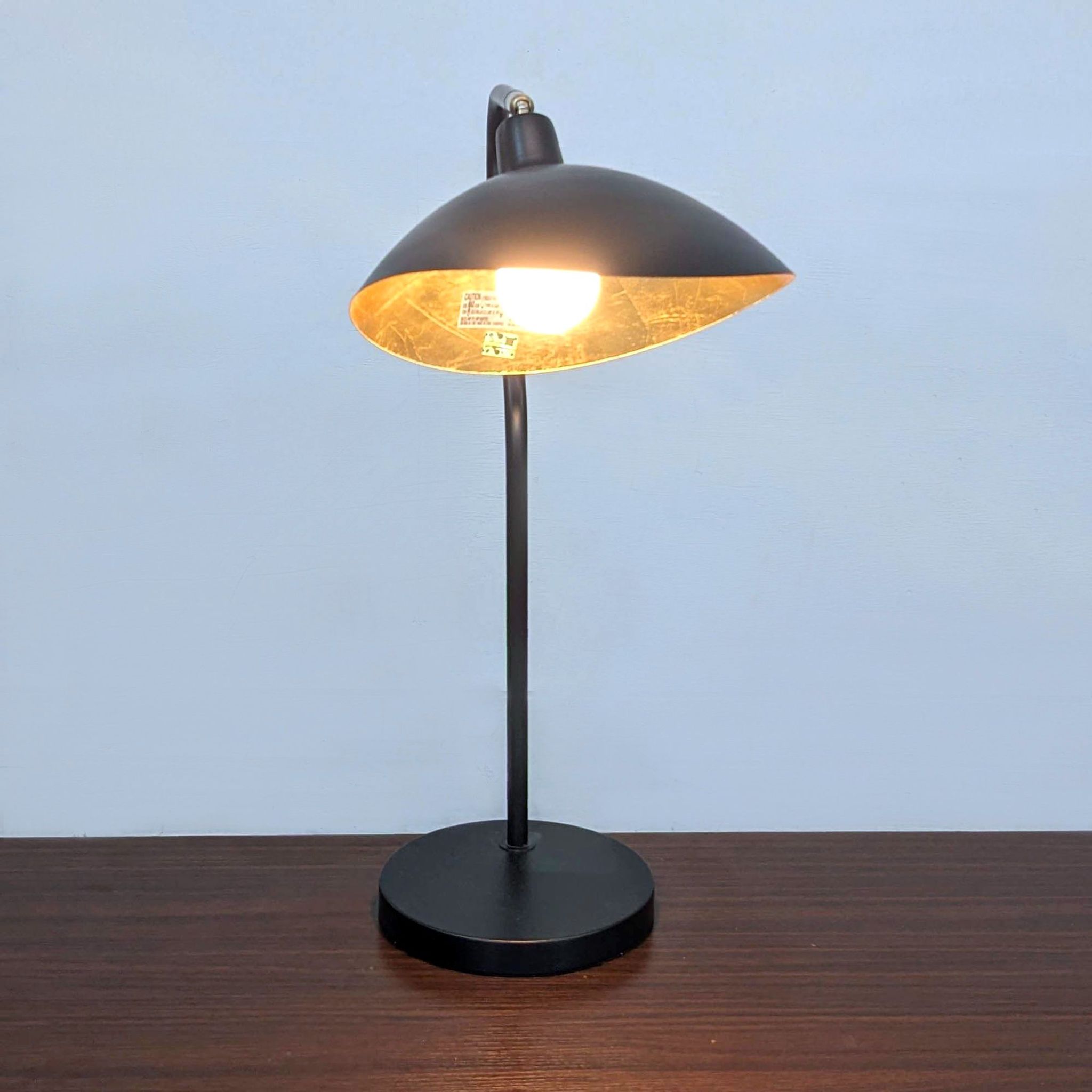 Black and gold Safavieh table lamp with mid-century design, illuminated, highlighting adjustable height feature.