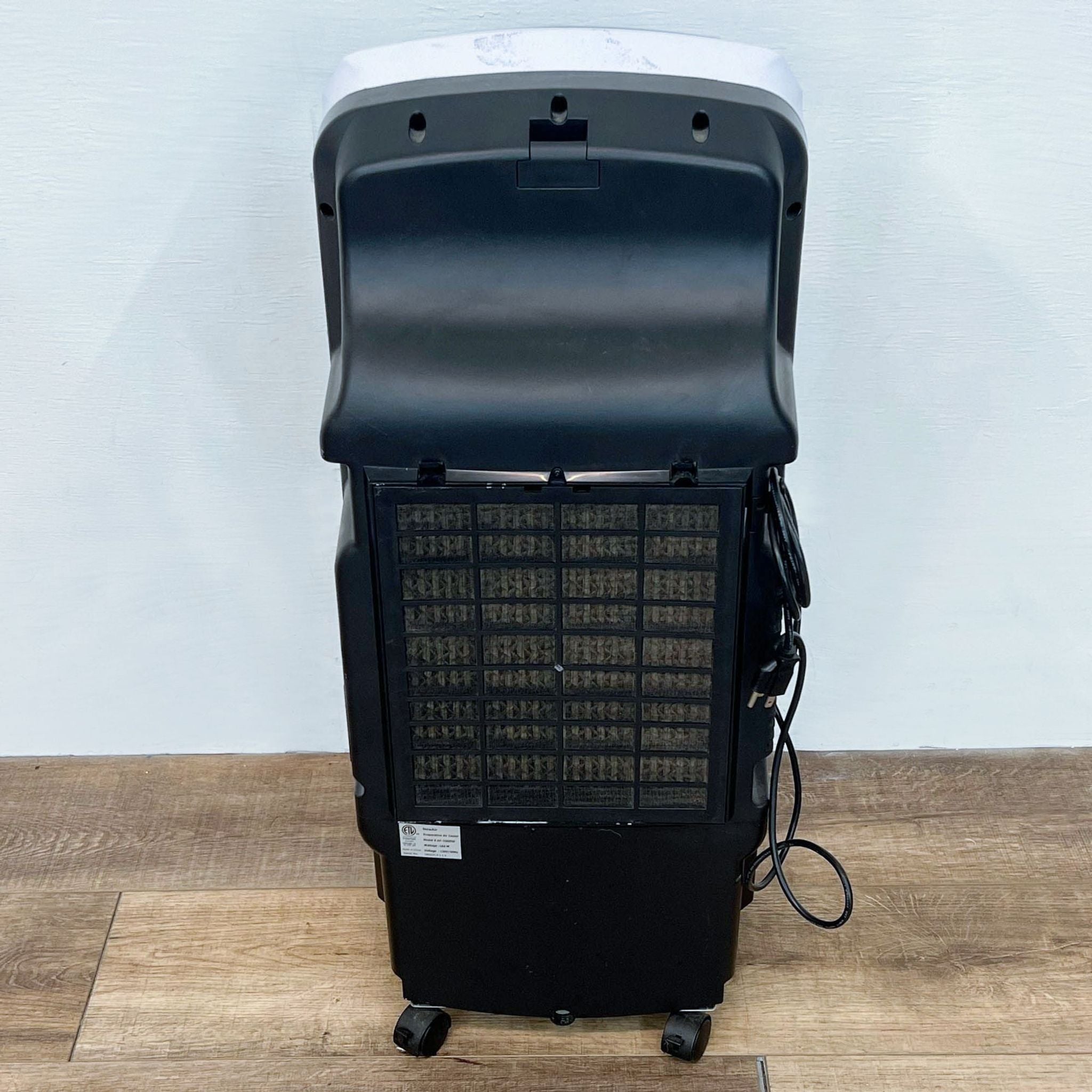 Rear view of a NewAir portable air cooler showing the black back panel, filters, and power cord on a wooden floor.