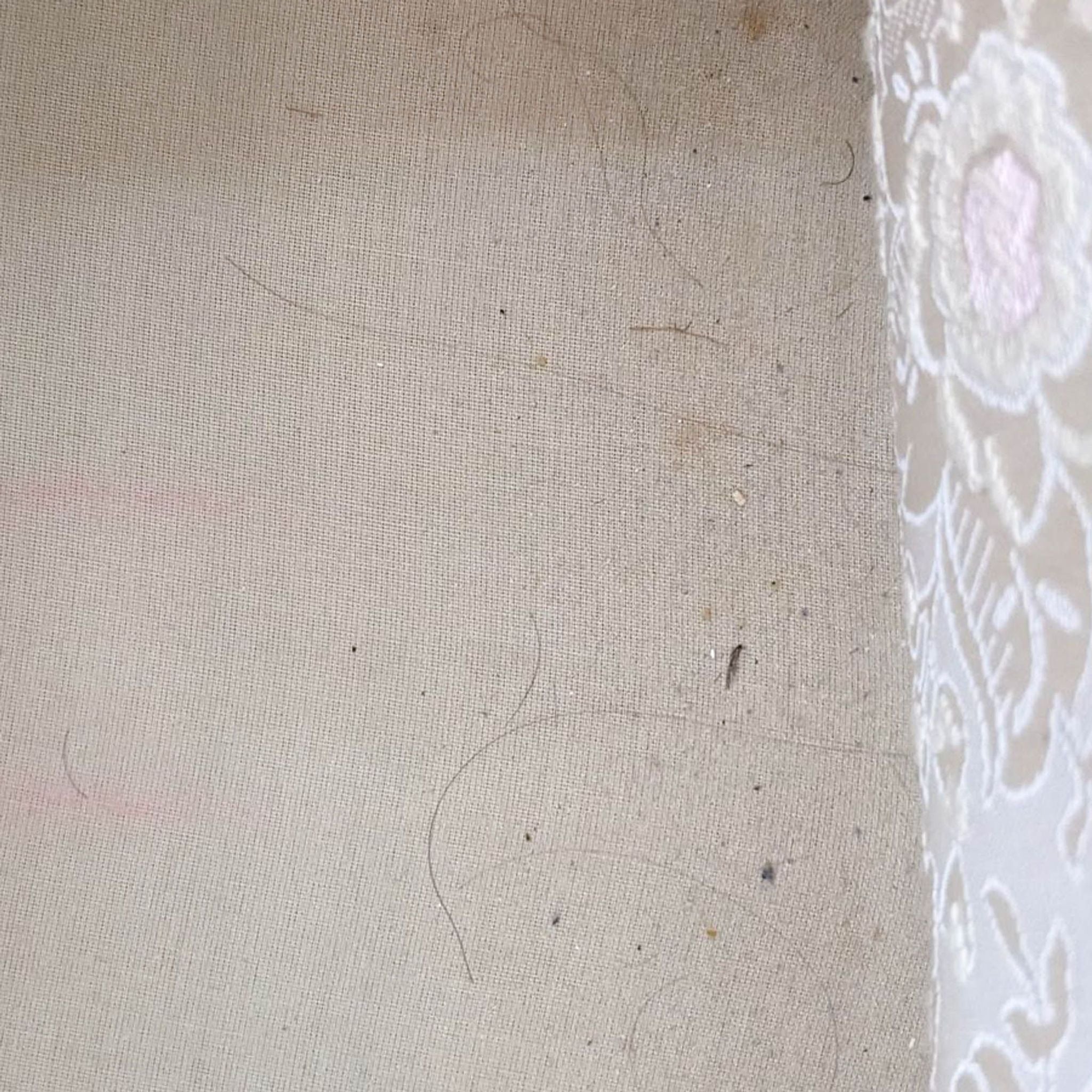2. Close-up of a vintage armchair’s fabric showing wear and stains on the beige embossed upholstery.