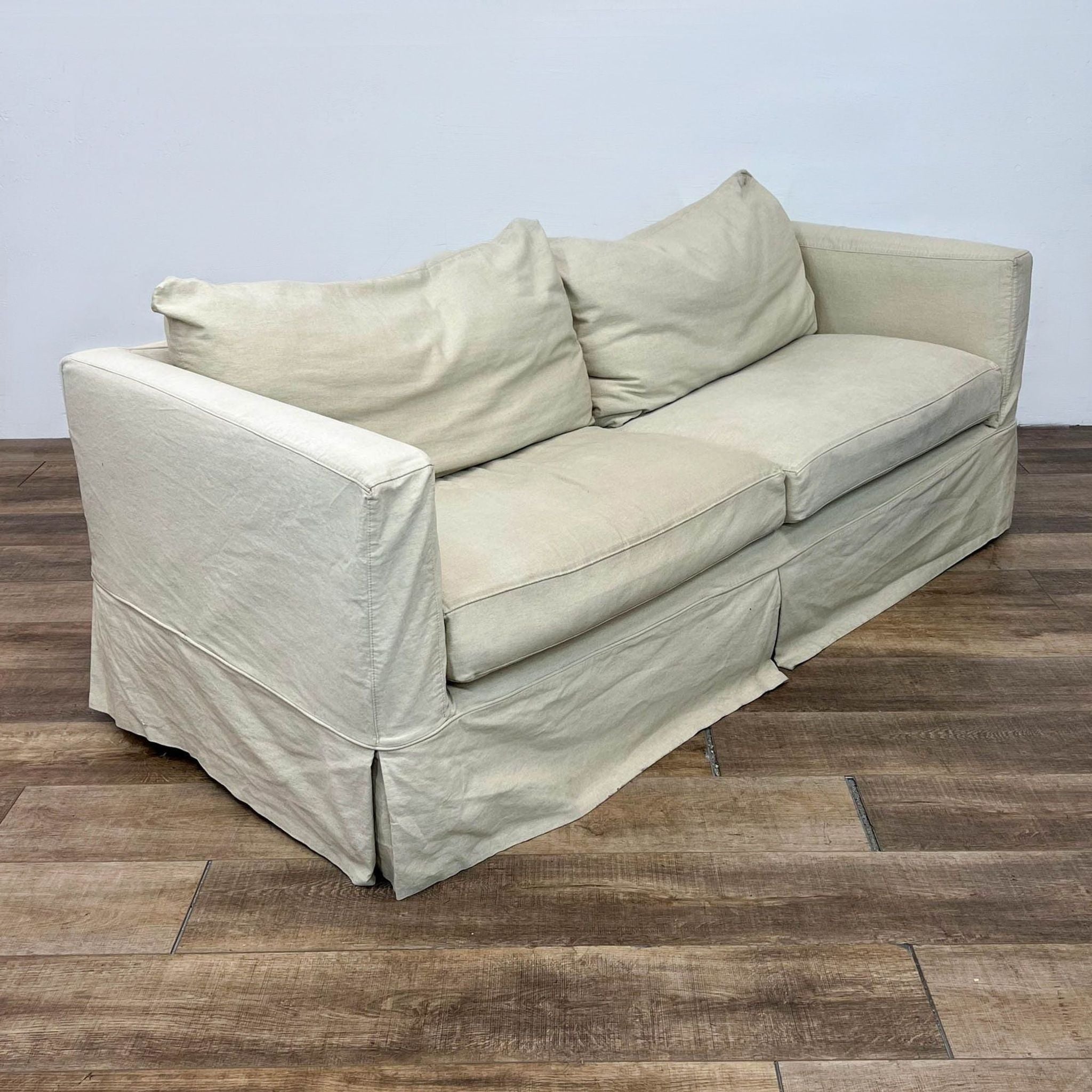 Angled view of beige Canvas 3-seat sofa with shabby chic style and track arms by Crate & Barrel in a room with wooden flooring.