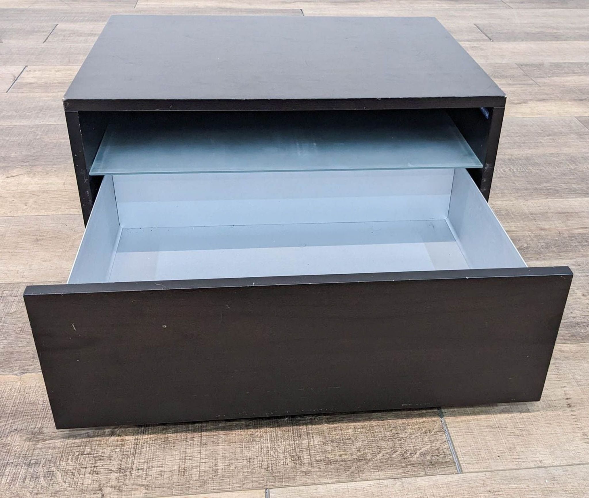 Top-down view showing the open compartment of a dark-colored Reperch end table on a wooden floor.