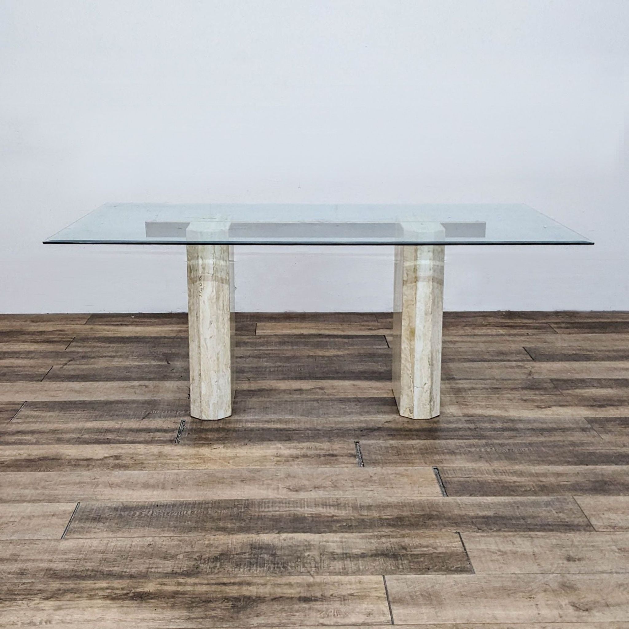 Contemporary Reperch dining table showcasing a clear glass surface with metal support and dual travertine pedestals.