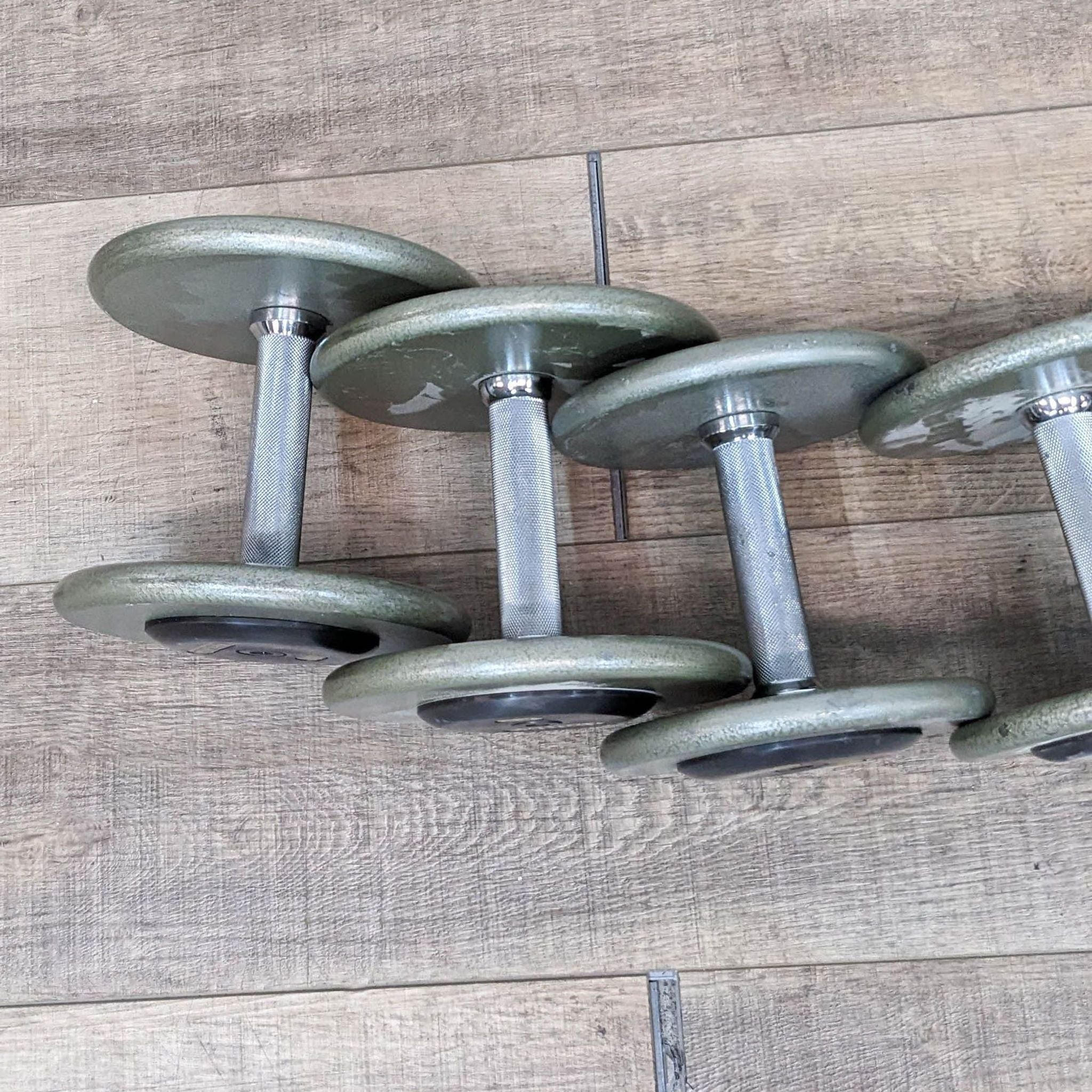 Three Ivanko dumbbells with metal handles and green plates on a wooden floor.