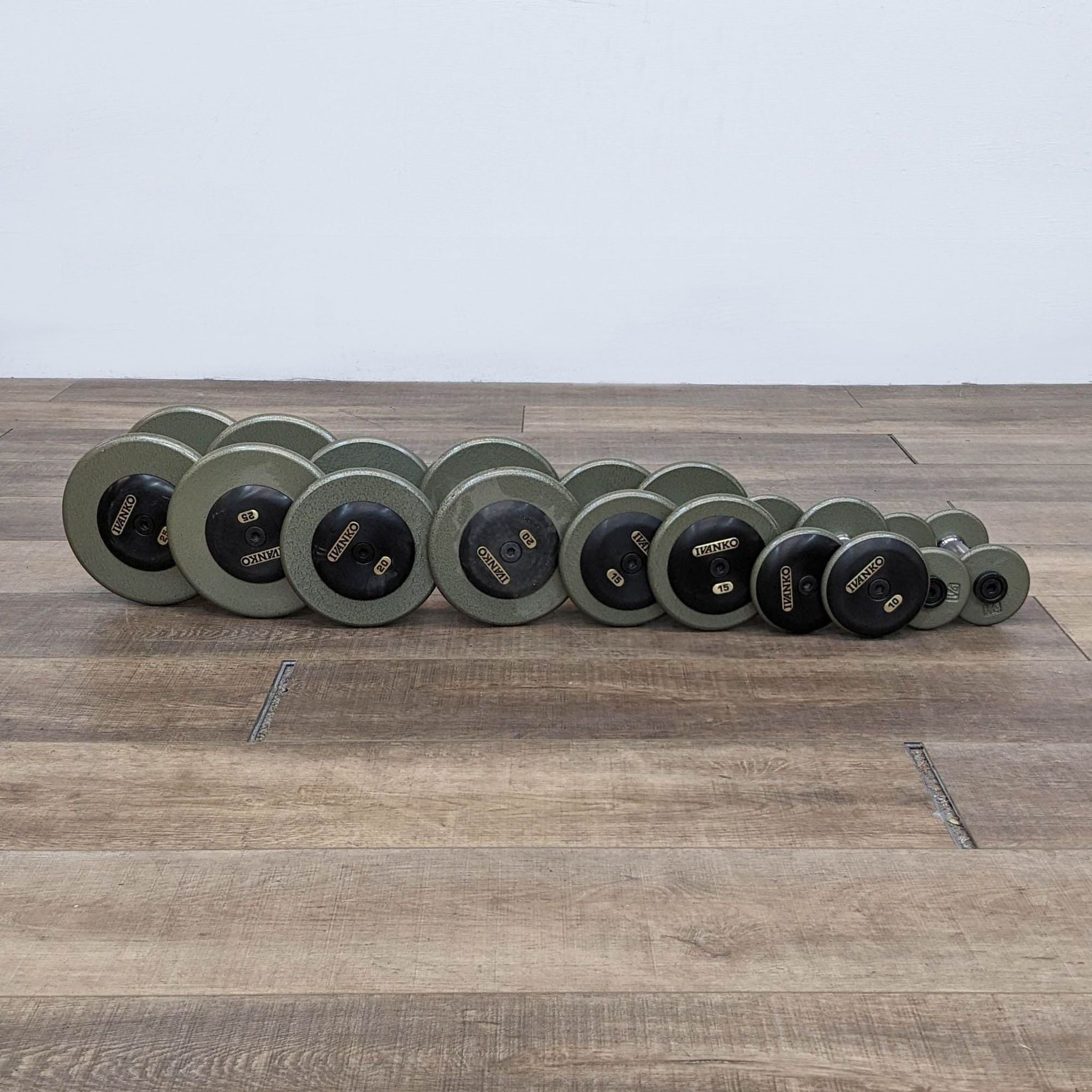 A row of Ivanko branded dumbbells on a wooden floor, in ascending order by size.