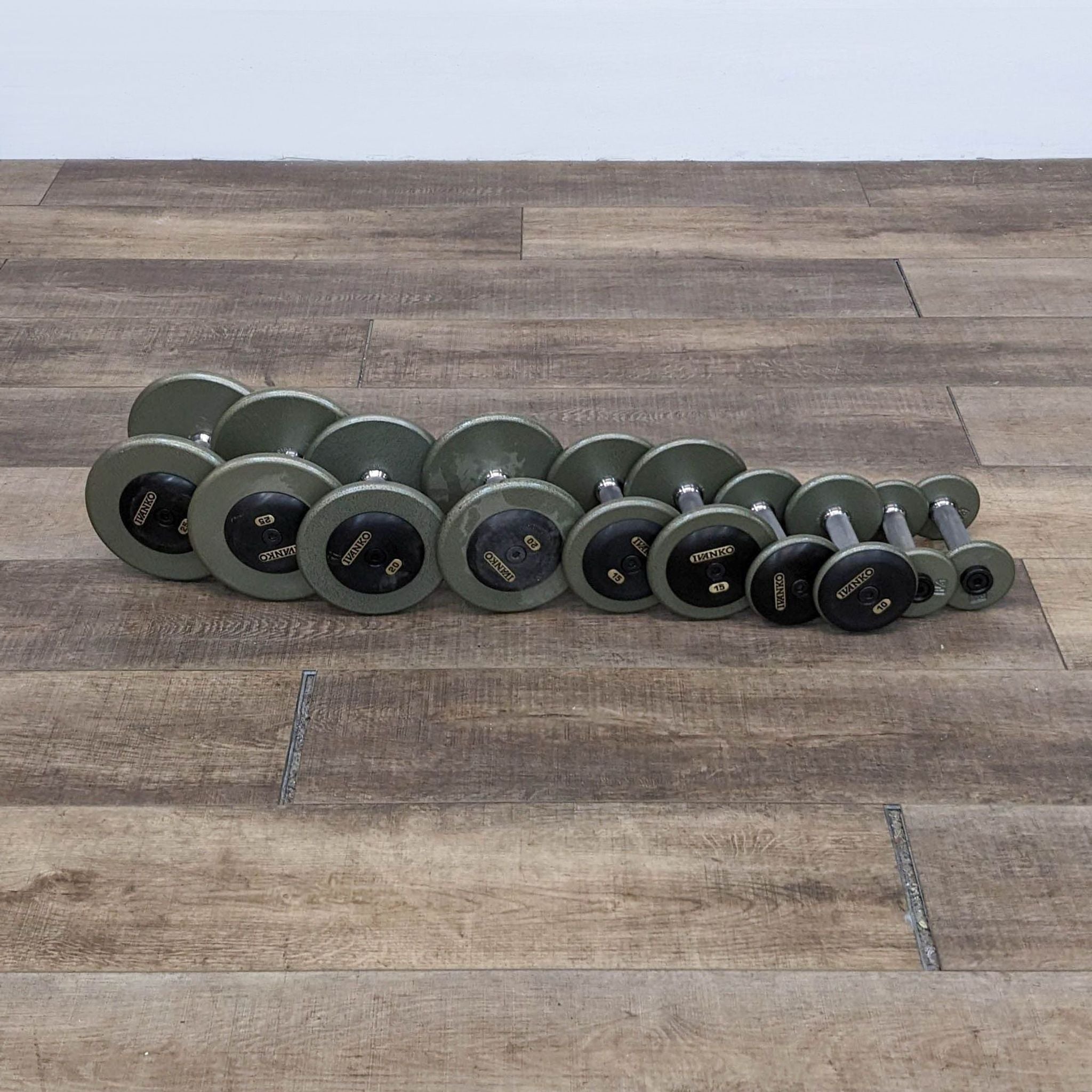 Ivanko gym dumbbells neatly lined up, showcasing different weights on a textured wooden surface.