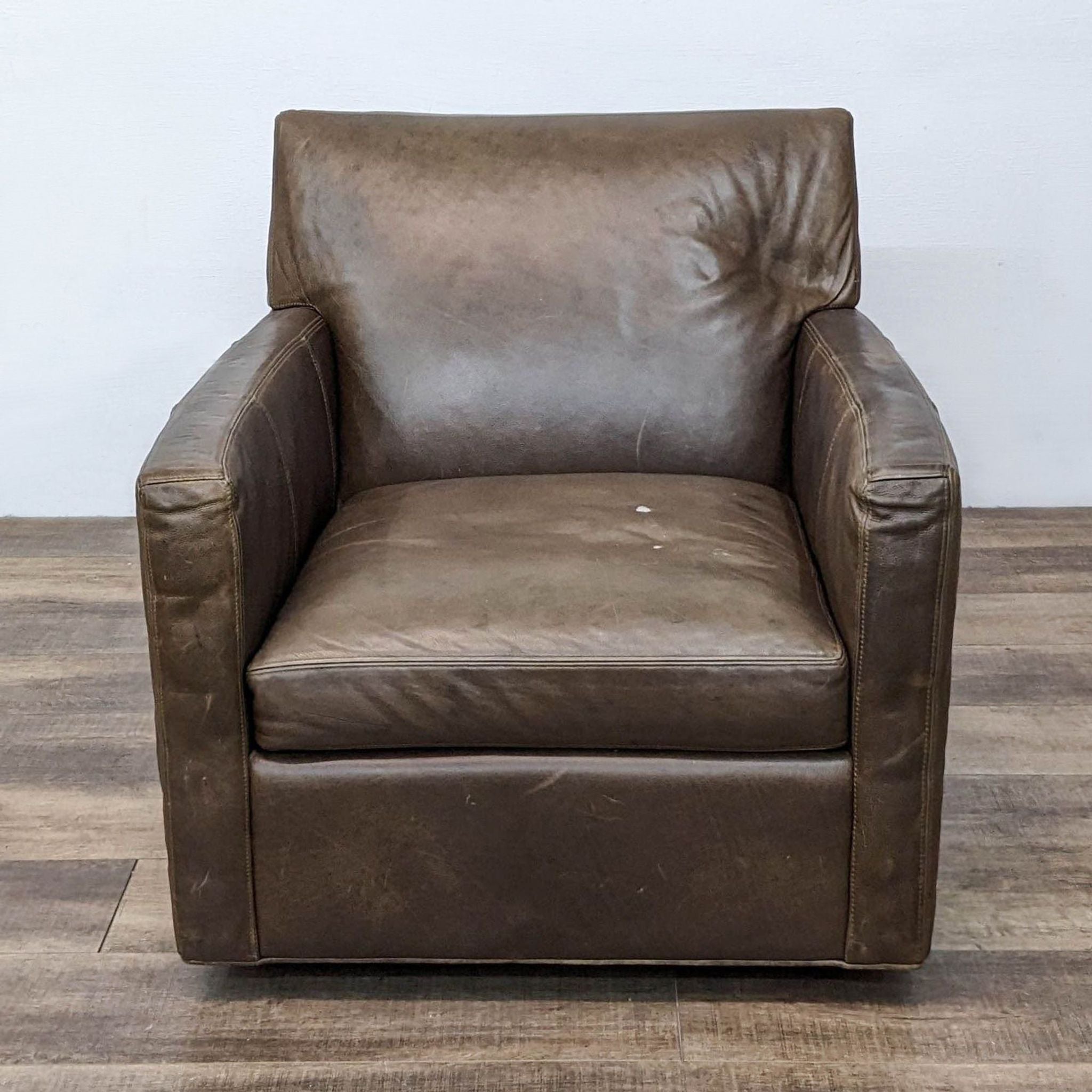 Front view of a Crate & Barrel brown leather lounge chair with visible wear on a wooden floor.