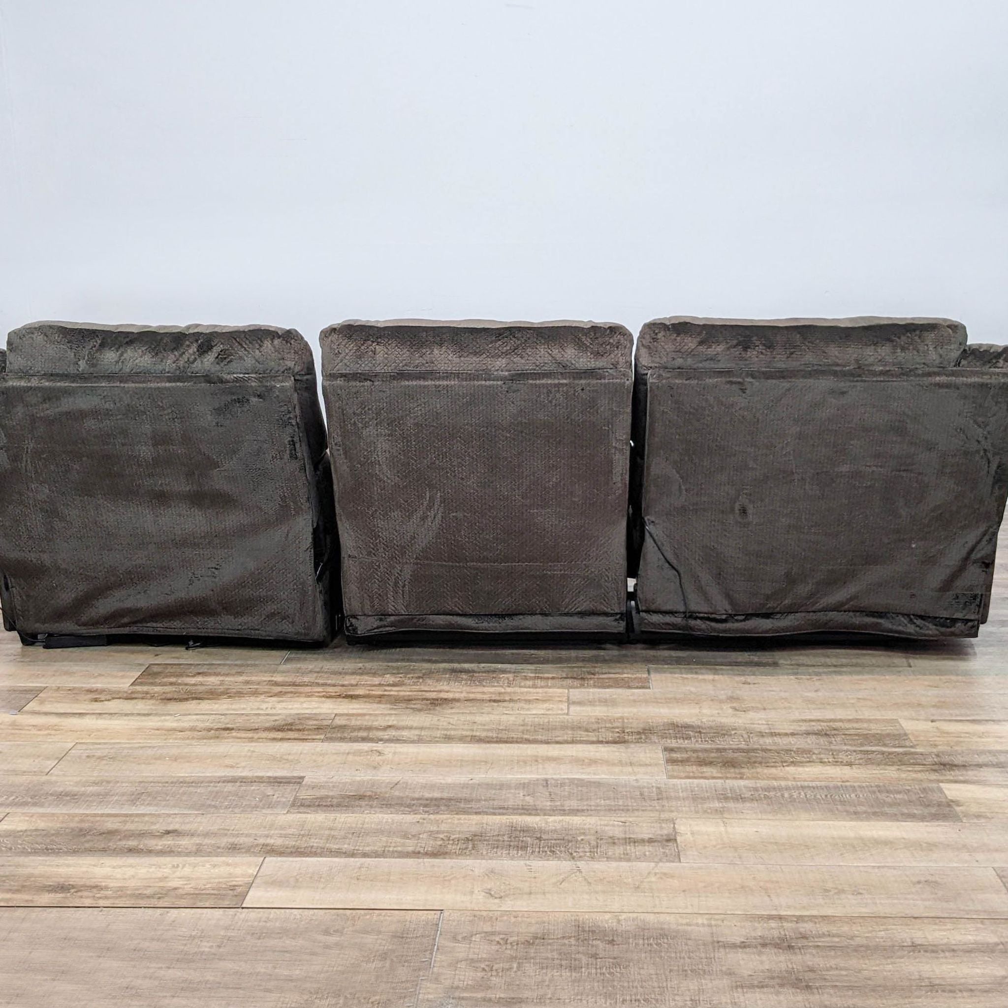 Back of a brown Reperch fabric sectional with power reclining ends and pillow top arms against a white wall.