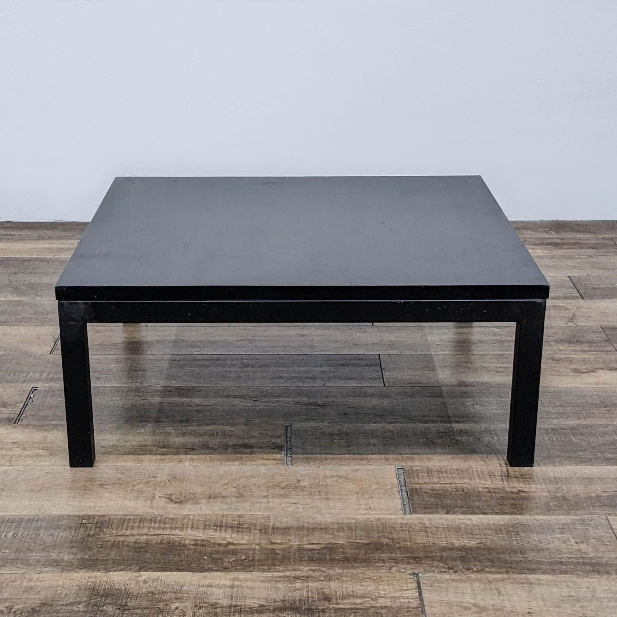 Room & Board brand Parsons style black coffee table on a wooden floor.