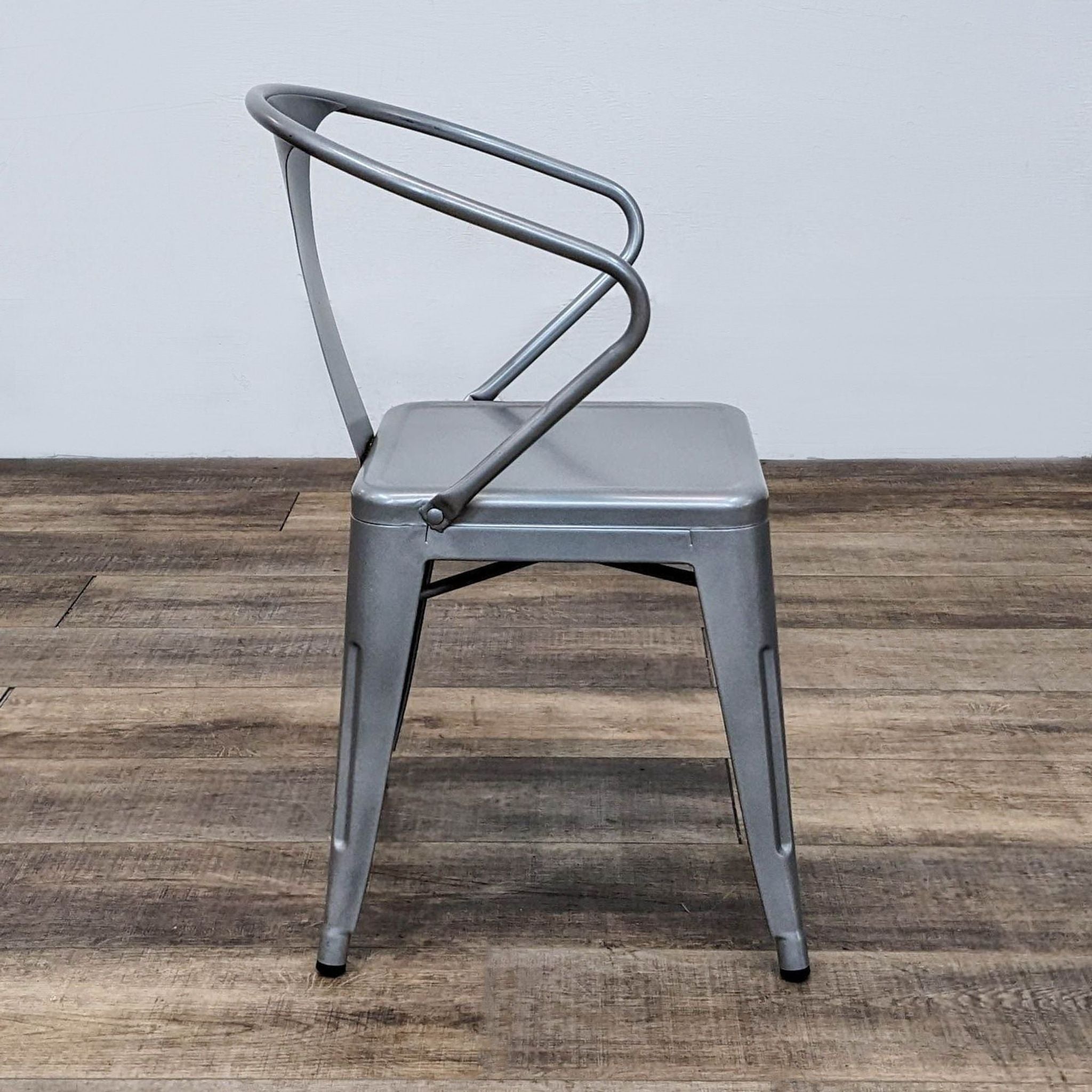Side angle view of a gunmetal powder-coated Dimensions Tabouret chair showcasing industrial modern design, on a wooden floor.