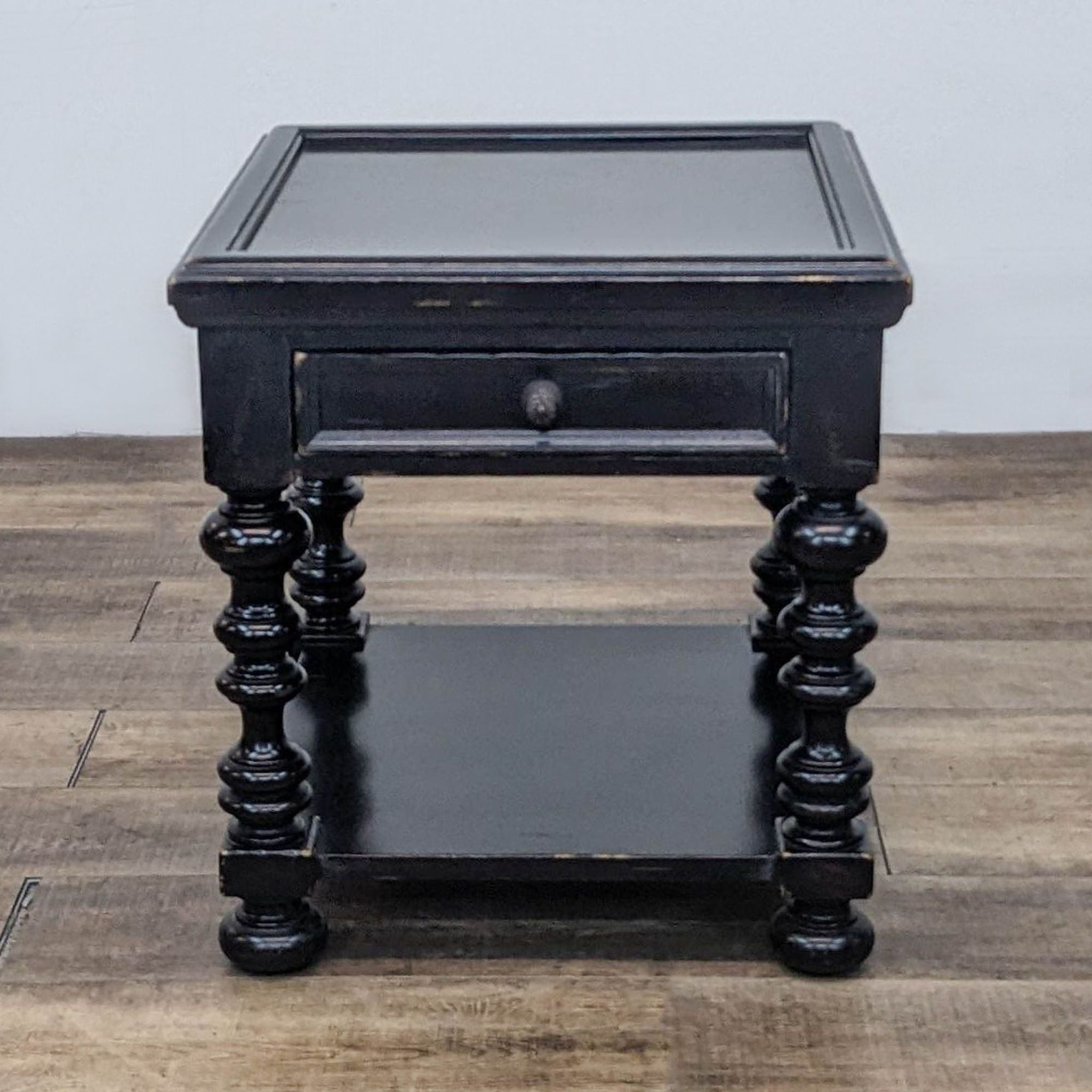 Tommy Bahama Kingstown Explorer End Table in distressed black finish, featuring a drawer and lower shelf, with turned legs.