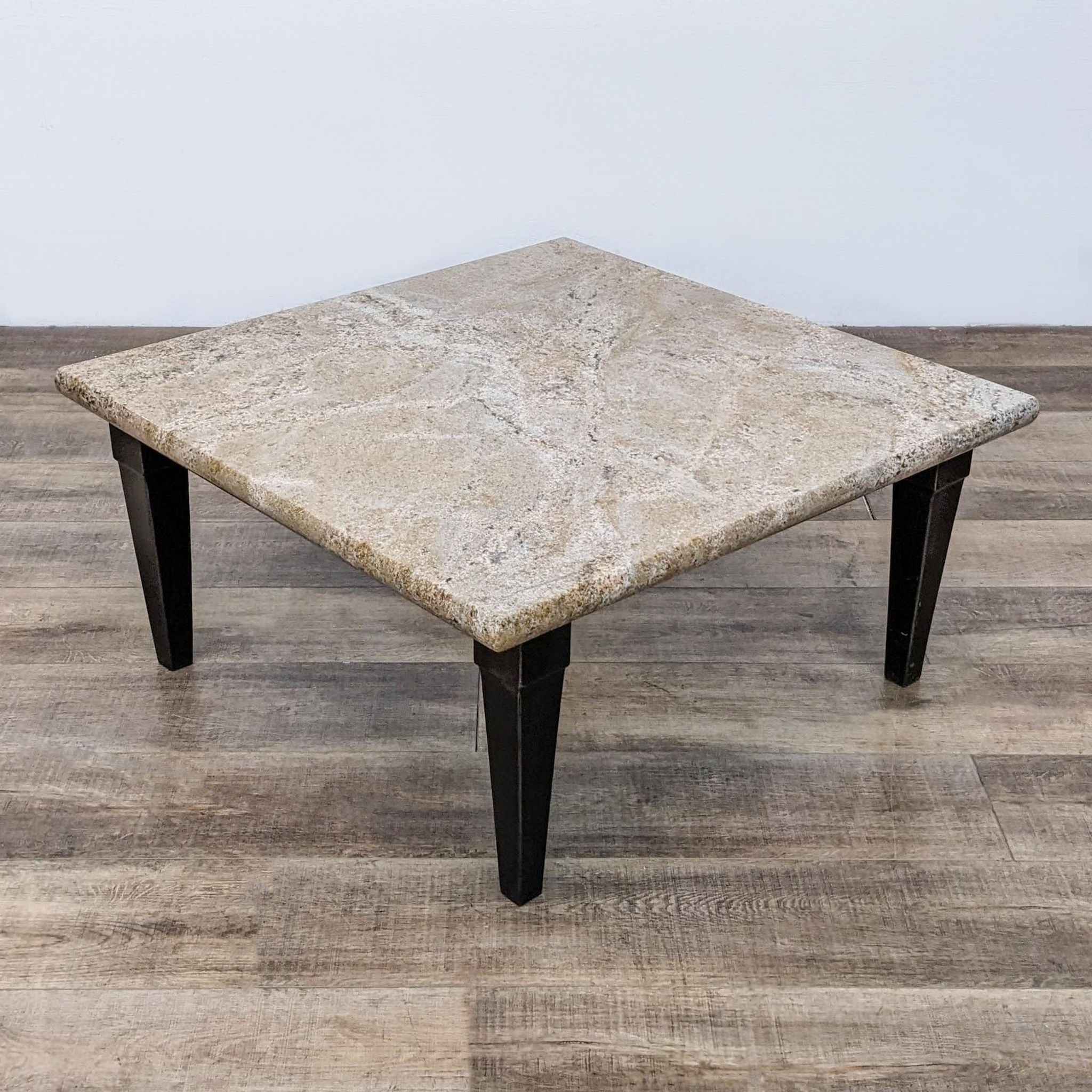 Square stone top coffee table by Reperch with a sturdy metal base, positioned on a wooden surface.