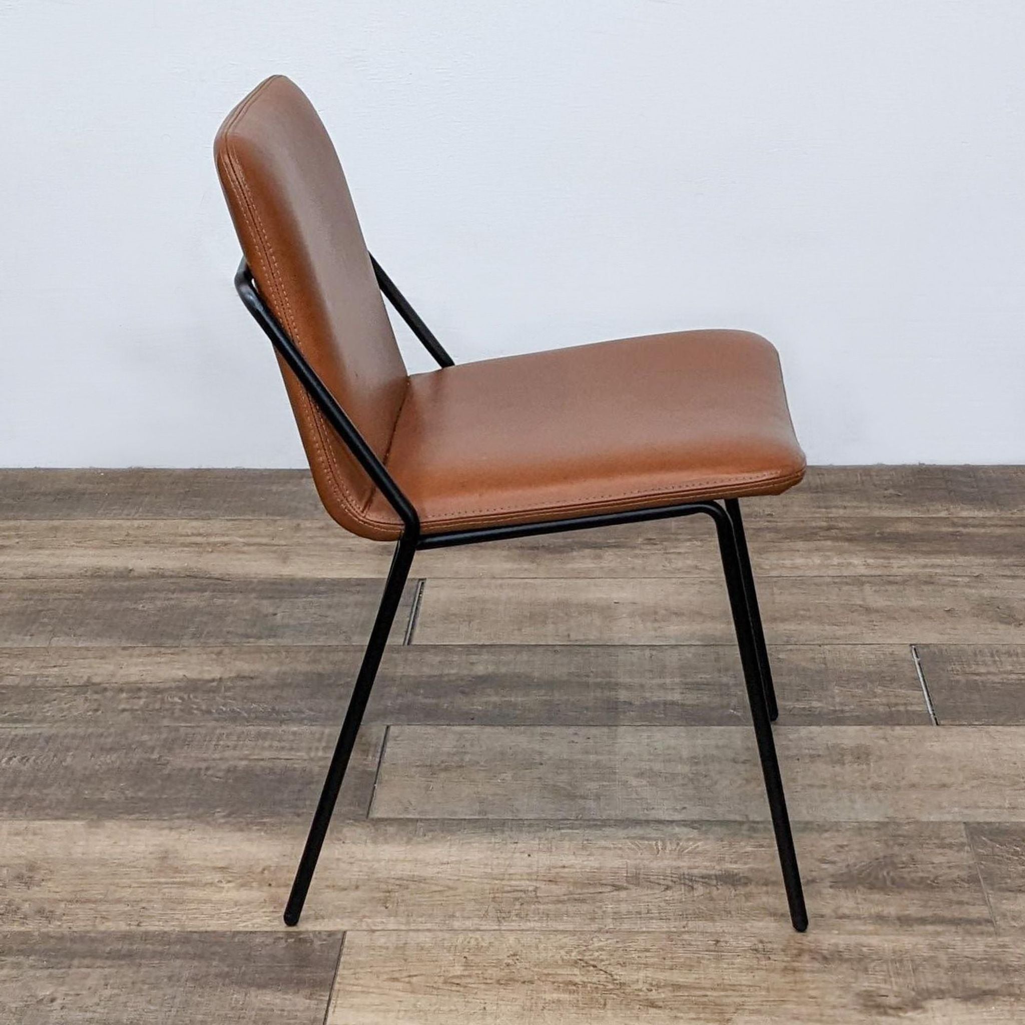 Angle view of Reperch contemporary dining chair with structural back leg and vegan leather seat against wall.